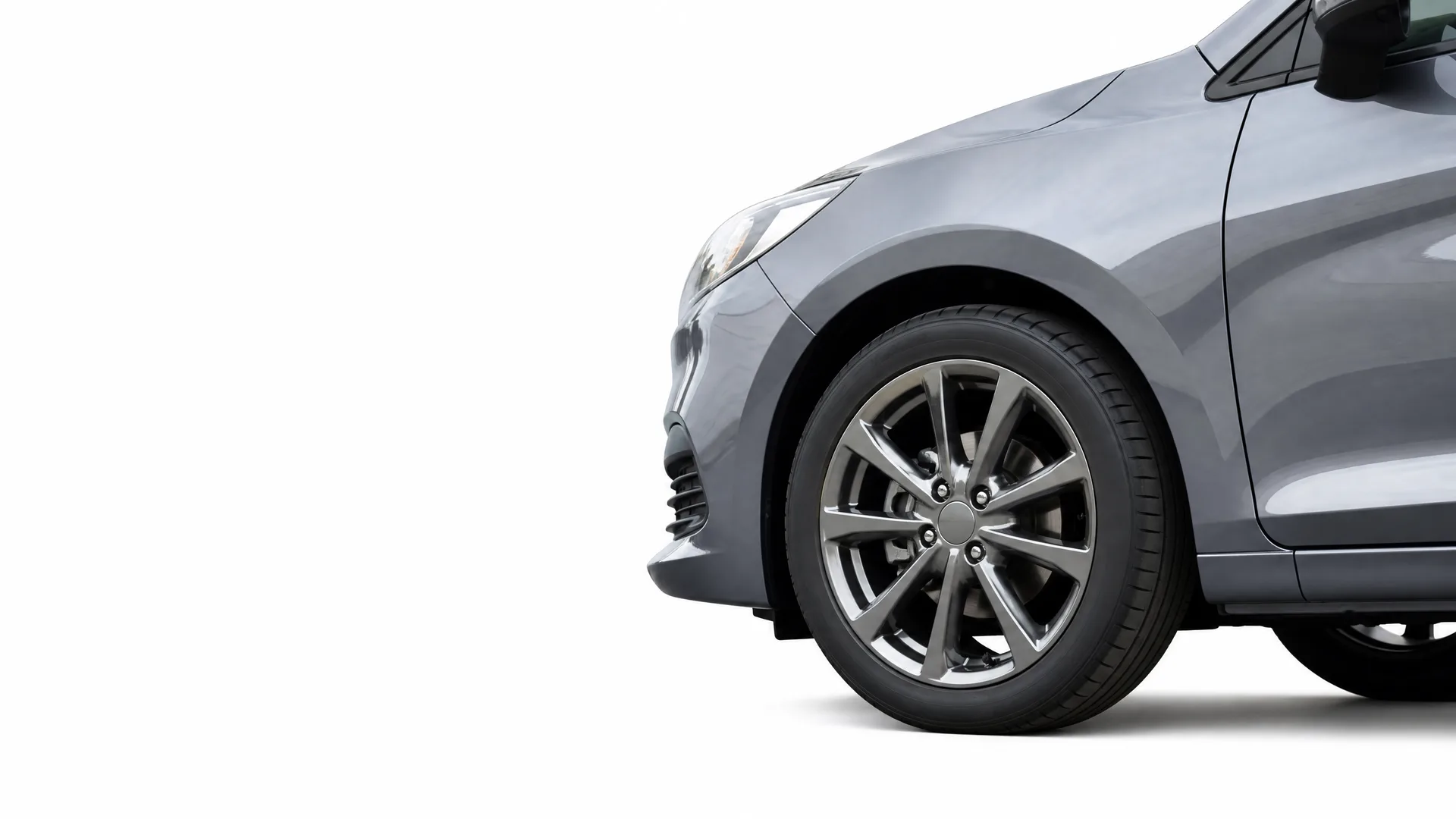 Front portion of a gray car, showing the front wheel with alloy rim, bumper and headlight, isolated on a white background.