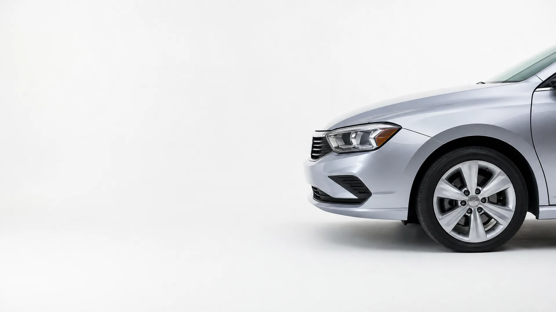 Front portion of a silver sedan, showing the headlight, grille, bumper and front wheel, against a plain white background.