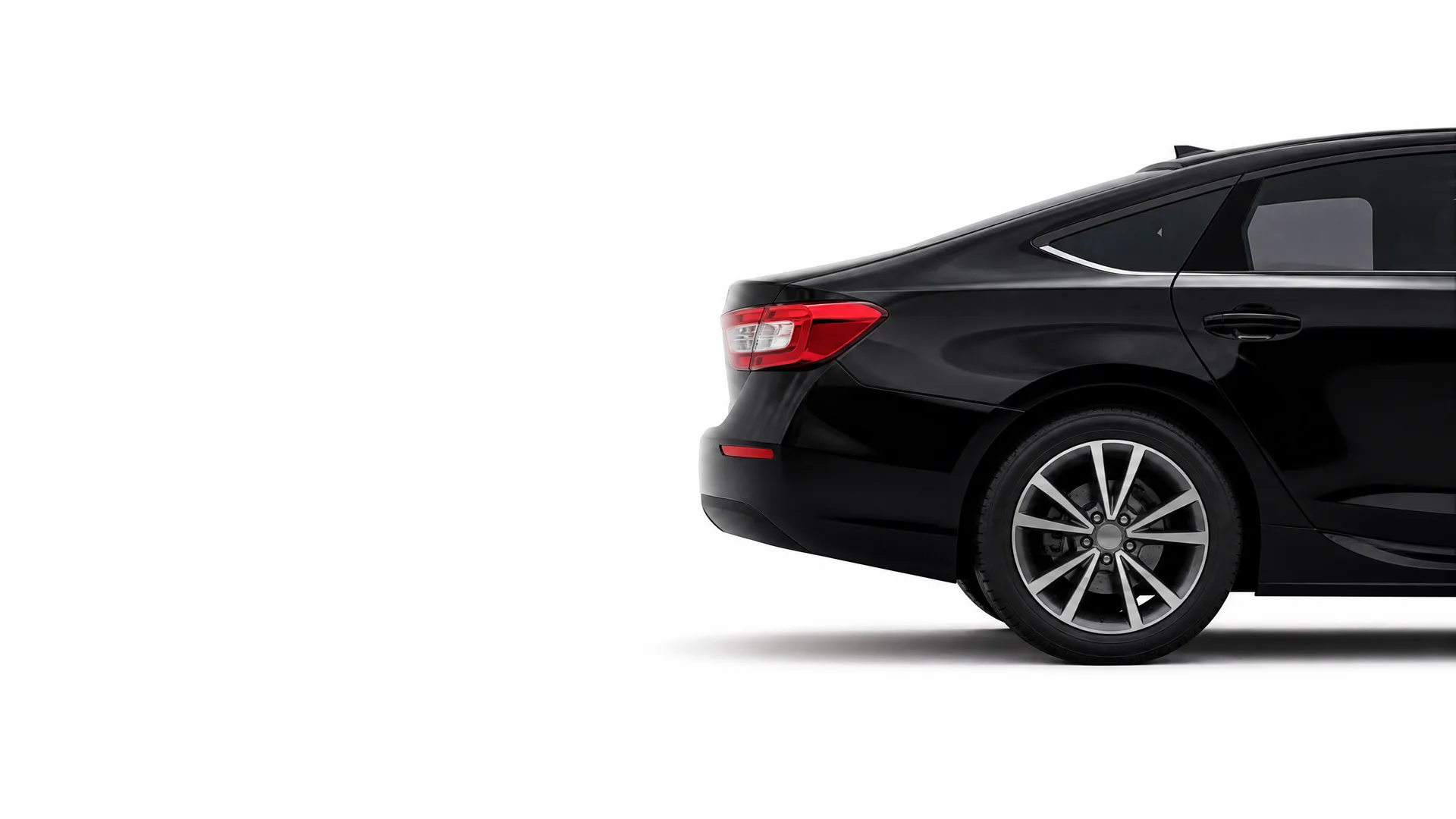 Rear half of a black four-door sedan with alloy wheel and red taillight, shown against a plain white background.