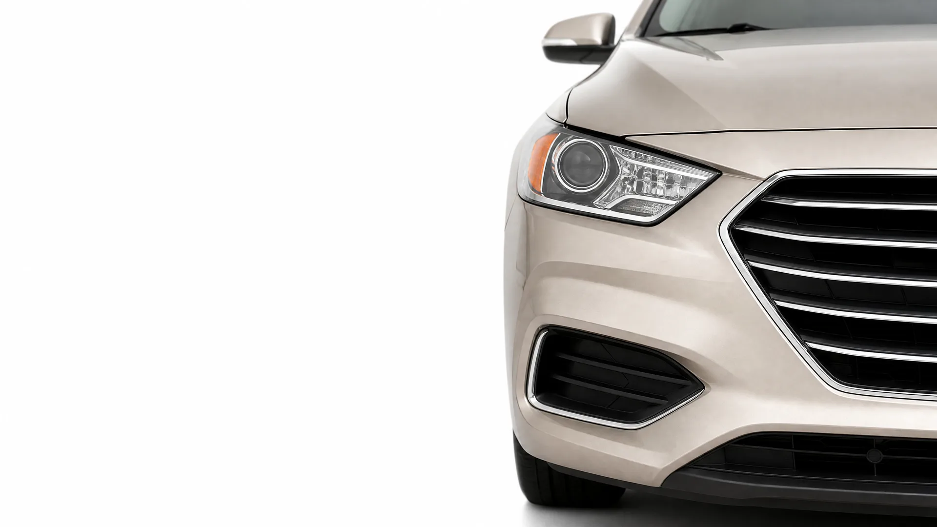 Front left portion of a beige sedan, showing headlight, grille, fog lamp opening and side mirror, against a plain white background.