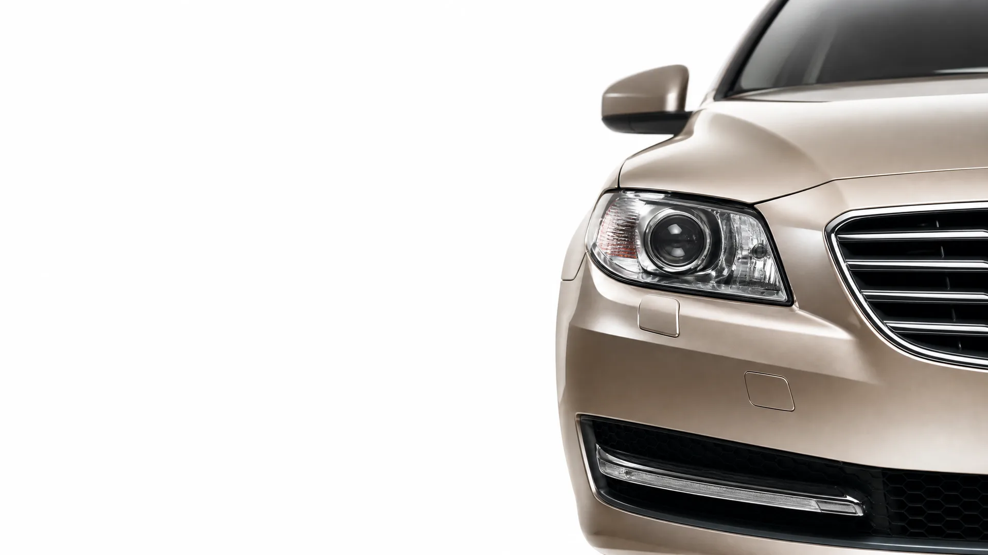 Close-up of the front right corner of a beige sedan, showing the headlight, grille, mirror and bumper against a white background.