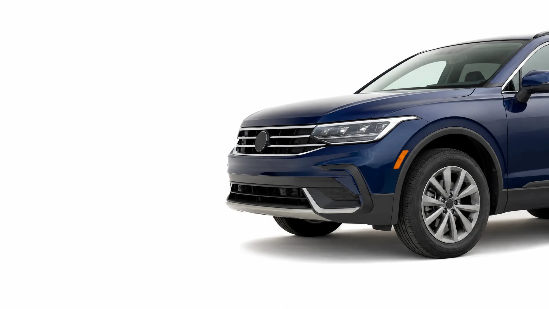Front half of a dark blue SUV photographed against a plain white background, showing the grille, headlight, front bumper and front wheel.