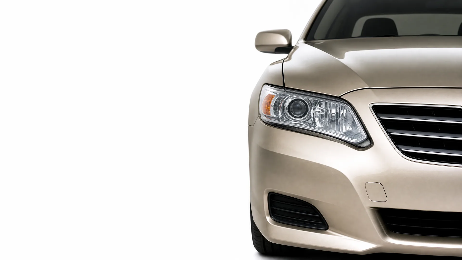 Front right portion of a beige sedan, showing the headlight, grille, bumper and side mirror, against a plain white background.