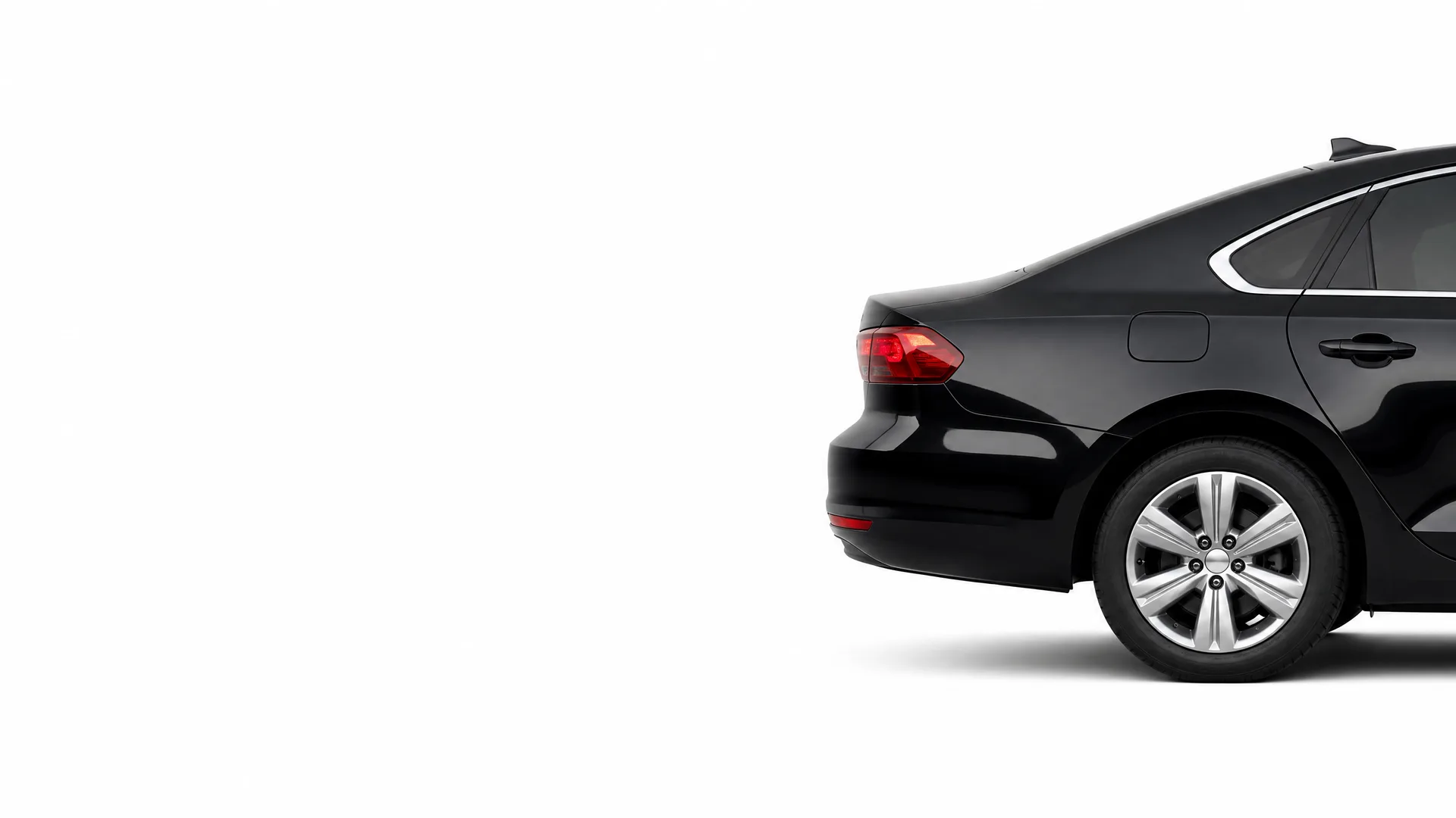 Rear three-quarter view of a black sedan's back half, including taillight, trunk and alloy wheel, on a plain white background.