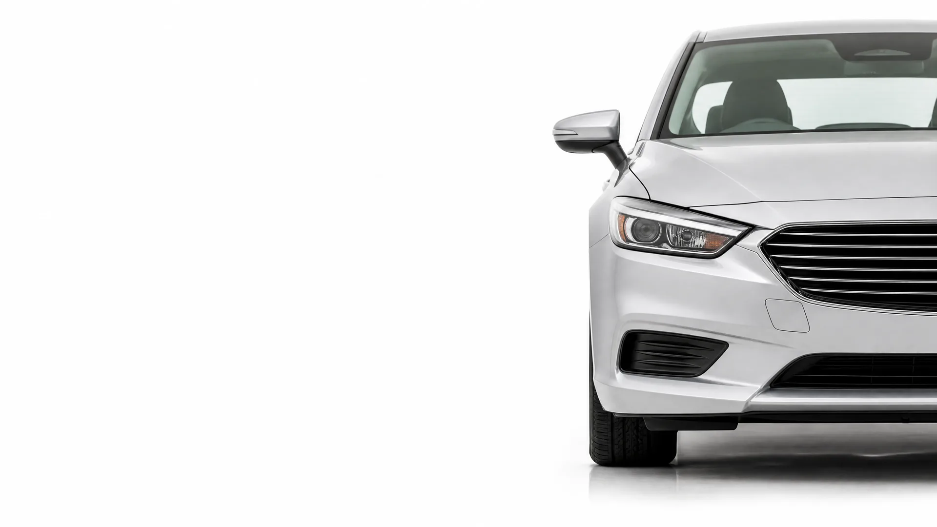 Front right portion of a white sedan on a plain white background, showing the headlight, grille, mirror and front wheel, with the rest of the frame empty.