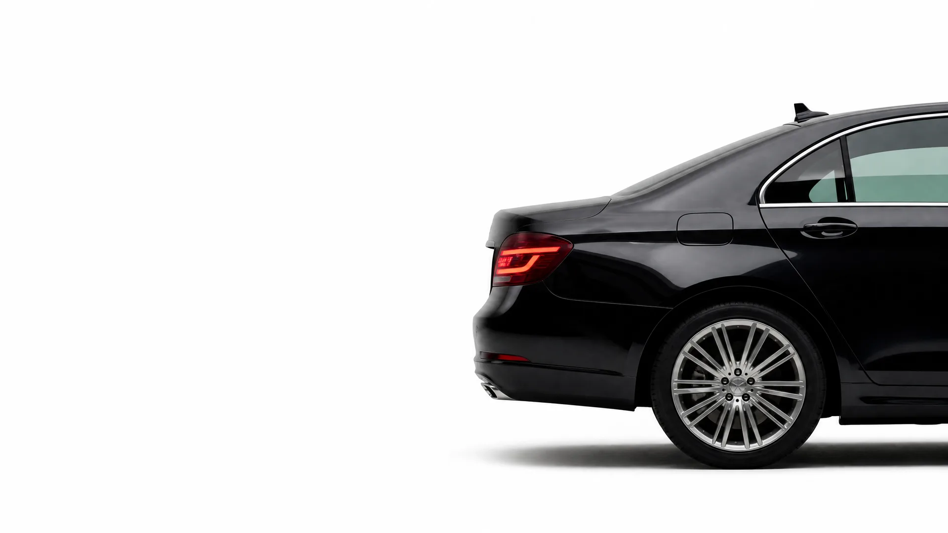 Rear three-quarter view of a black sedan's back half, showing the taillight, trunk, rear door and multi-spoke alloy wheel, against a plain white background.