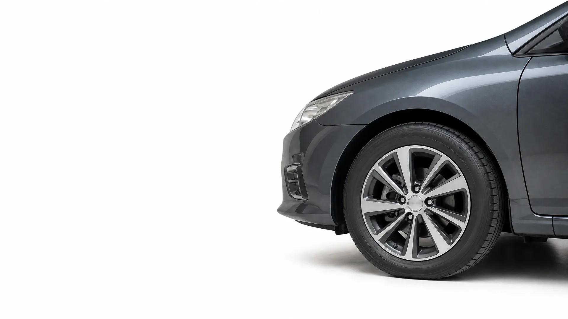 Front portion of a dark gray car, showing the front wheel with alloy rim, bumper, headlight and front door, against a white background.