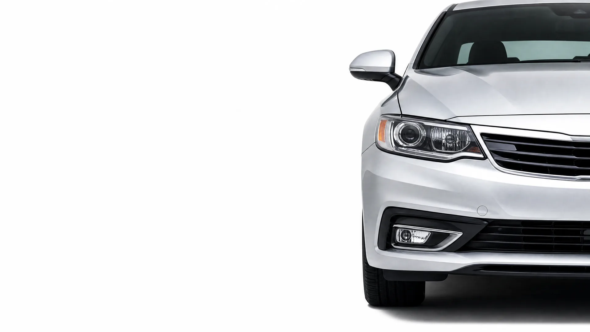 Front left portion of a silver sedan, showing the headlight, grille, bumper, fog lamp and side mirror, against a plain white background.