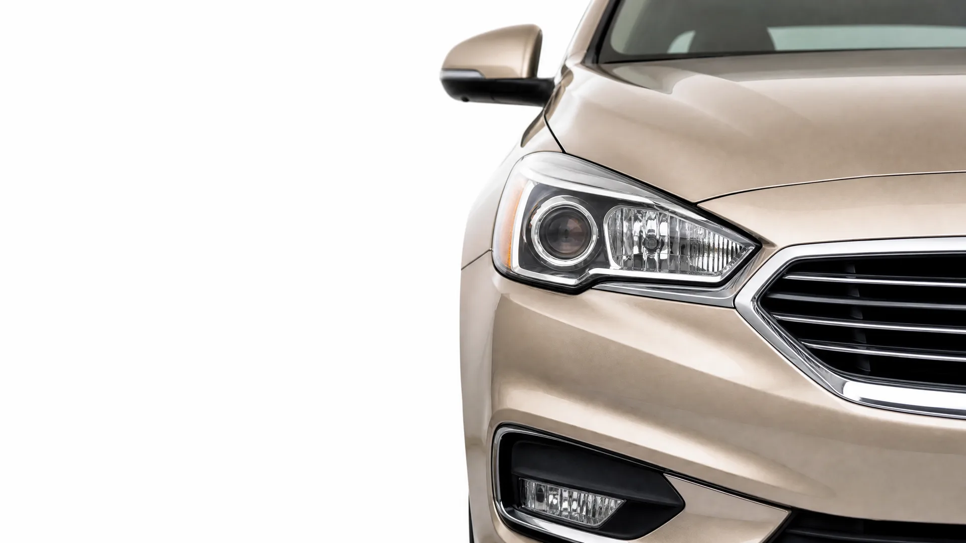 Close-up of the front right corner of a beige sedan, showing the headlight, grille, fog lamp and side mirror against a white background.