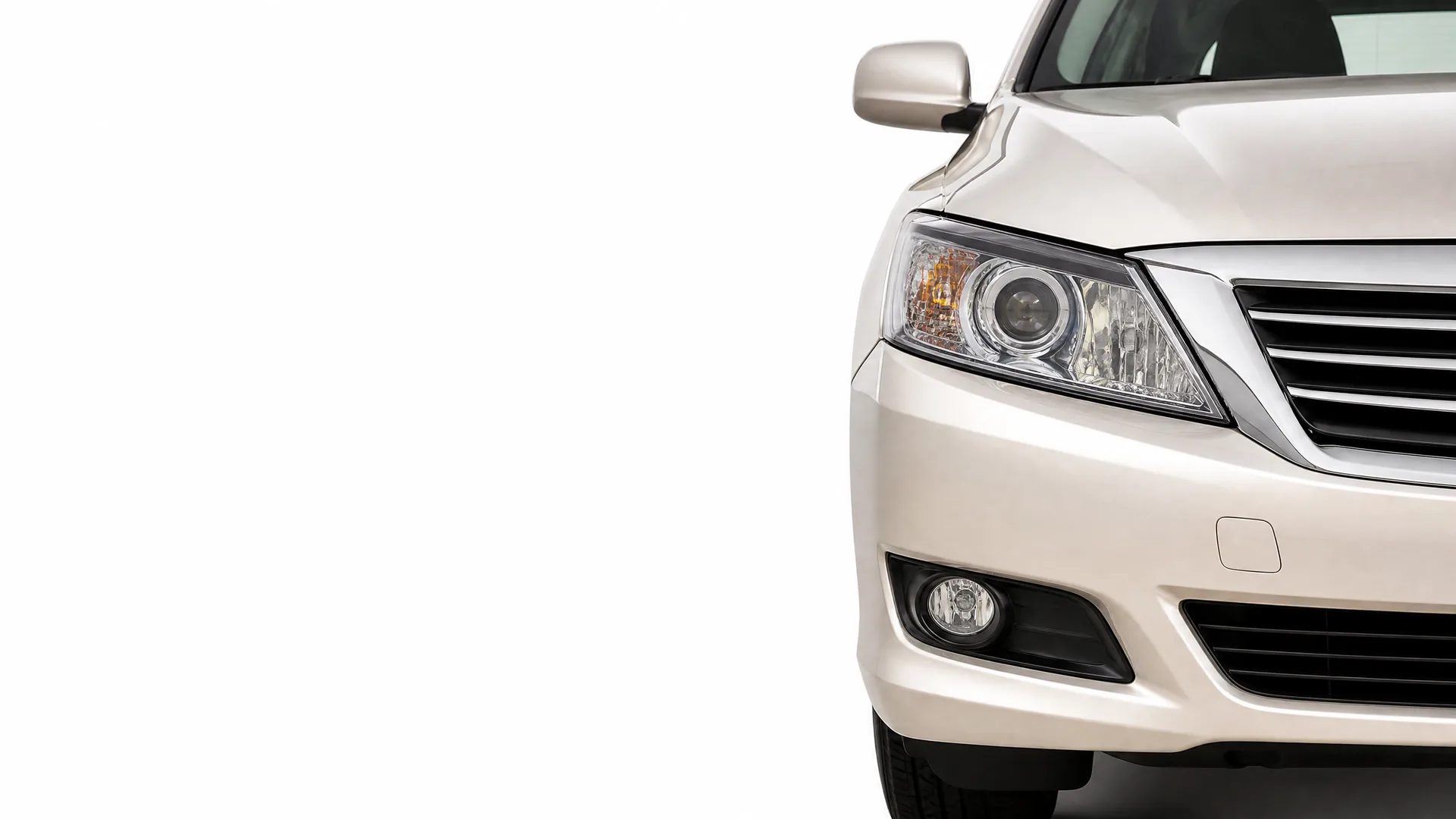 Front left portion of a light beige sedan, showing the headlight, grille, bumper, fog light and side mirror, isolated on a white background.