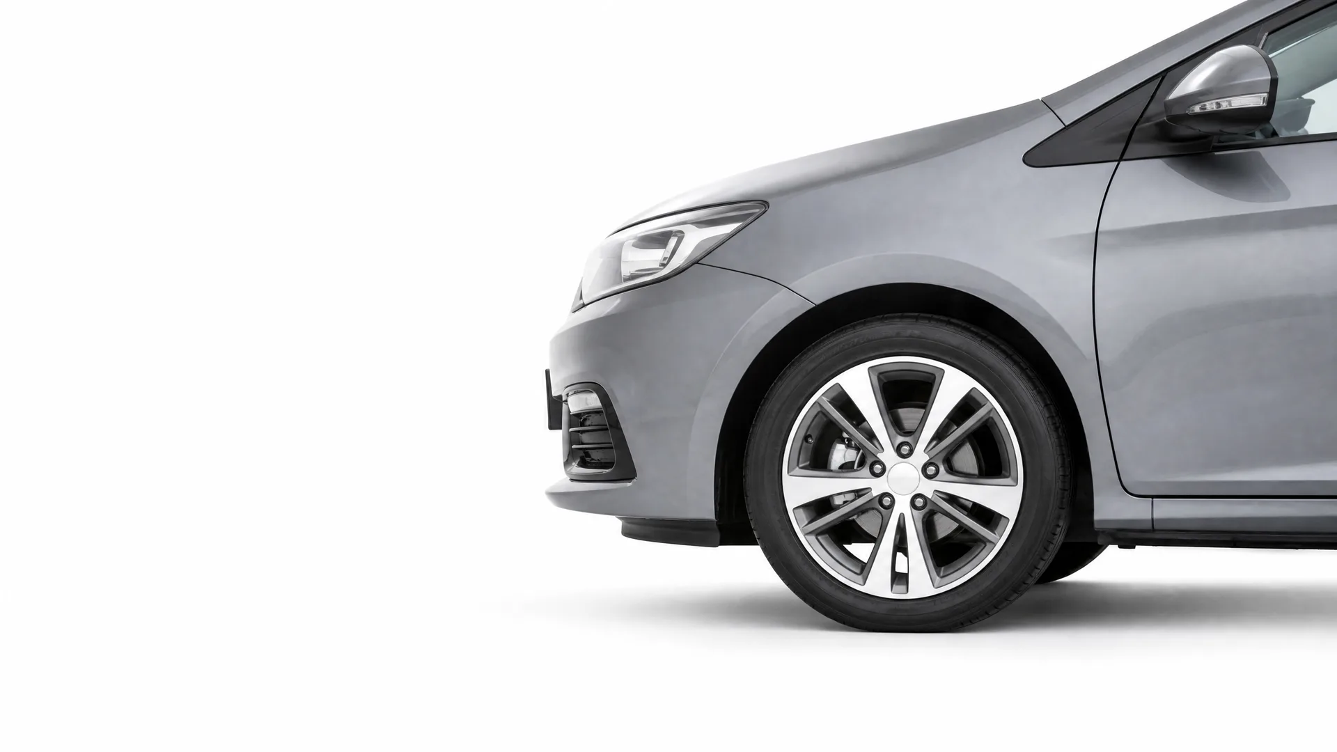 Front half of a grey hatchback car, showing the headlight, bumper, front wheel with alloy spokes and side mirror, against a plain white background.