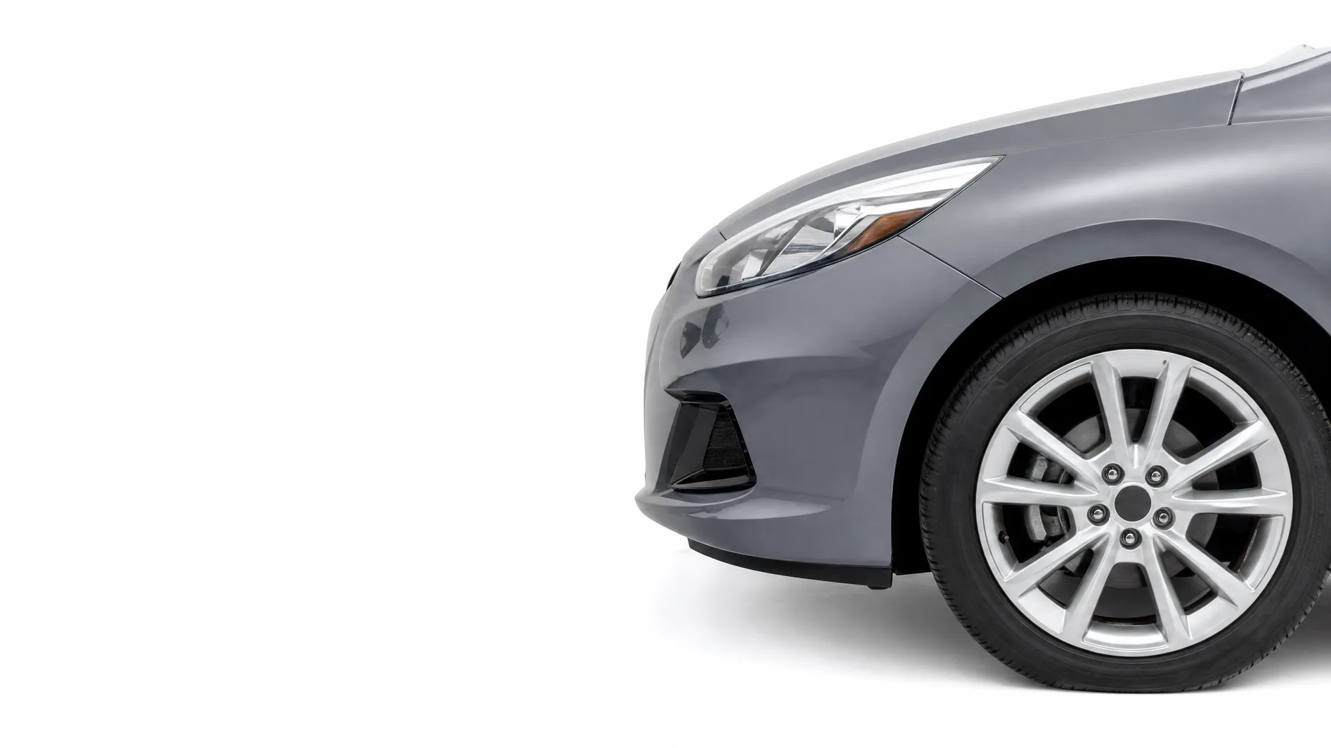 Front portion of a gray car, showing the bumper, headlight, fender and front wheel with a multi-spoke alloy rim, against a plain white background.