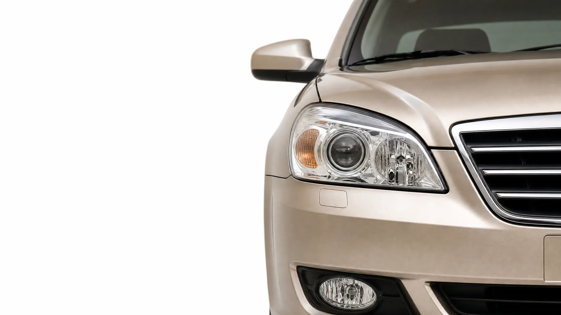 Close-up of the front left corner of a beige sedan, showing the headlight, grille, fog lamp, and side mirror against a white background.