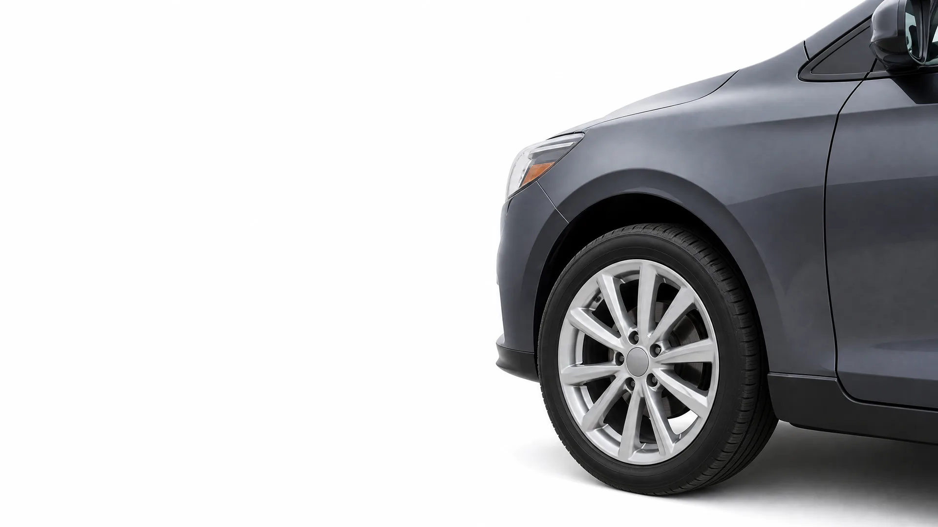 Front section of a dark gray car, showing the front wheel with alloy rim, fender, headlight and side mirror, against a white background.