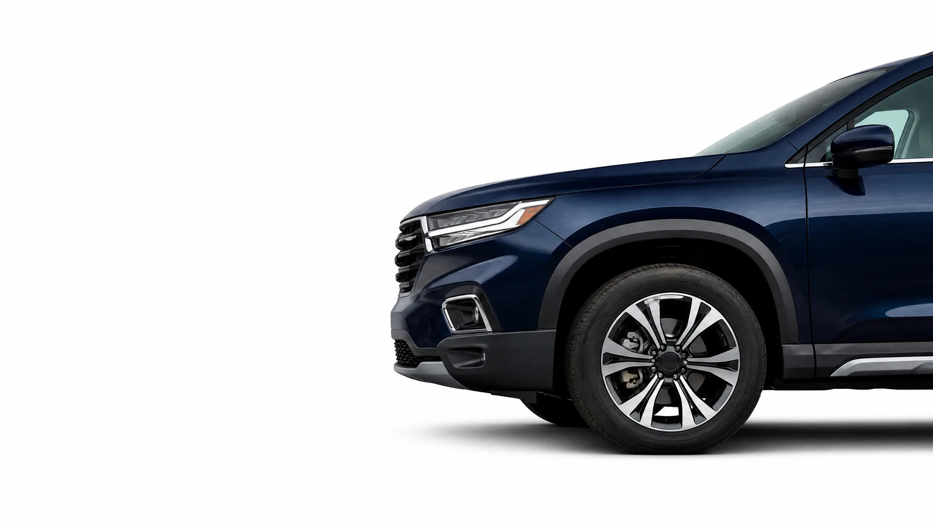 Front half of a dark blue SUV, showing the headlight, grille, front bumper and alloy front wheel, against a plain white background.
