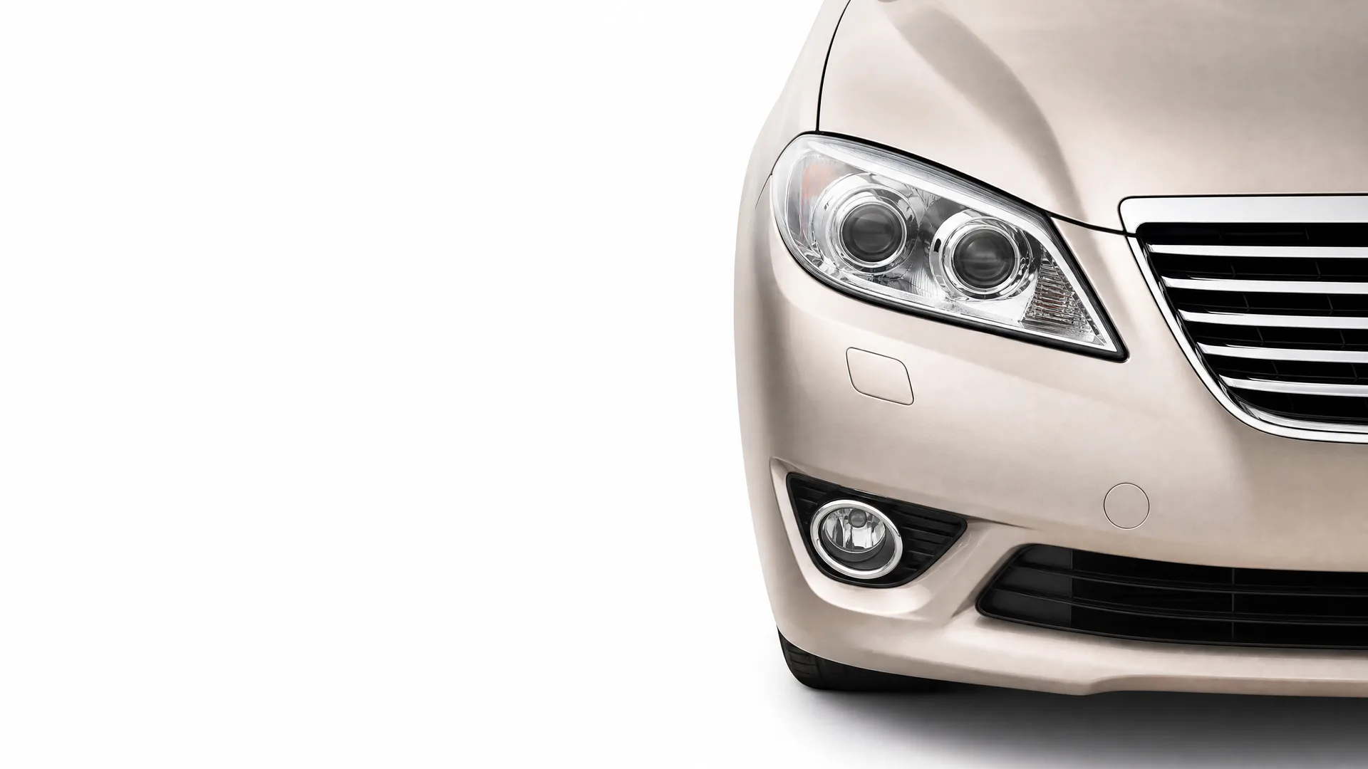 Front left portion of a beige sedan, showing the headlight, fog light, grille and bumper, against a plain white background.