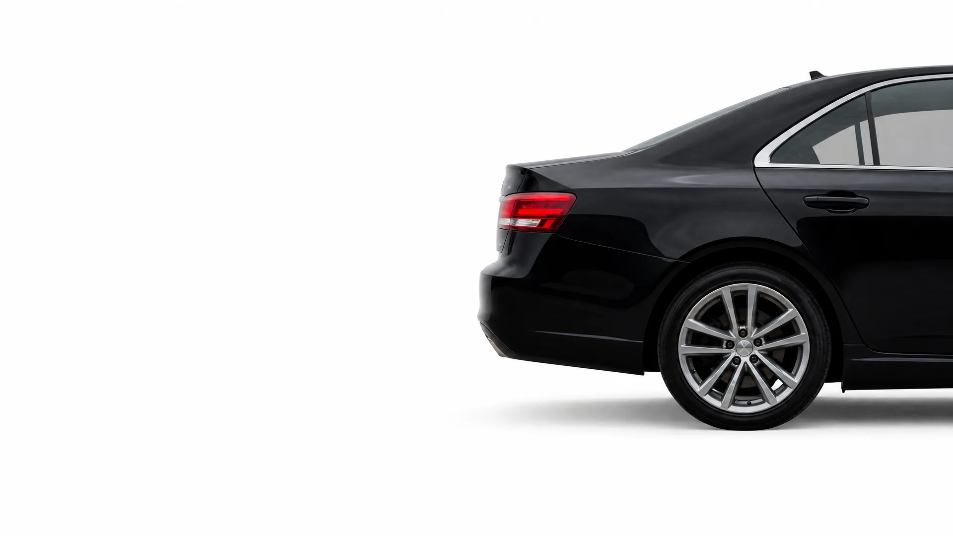 Rear three-quarter view of a black sedan's back half, including taillight and alloy wheel, against a plain white background.
