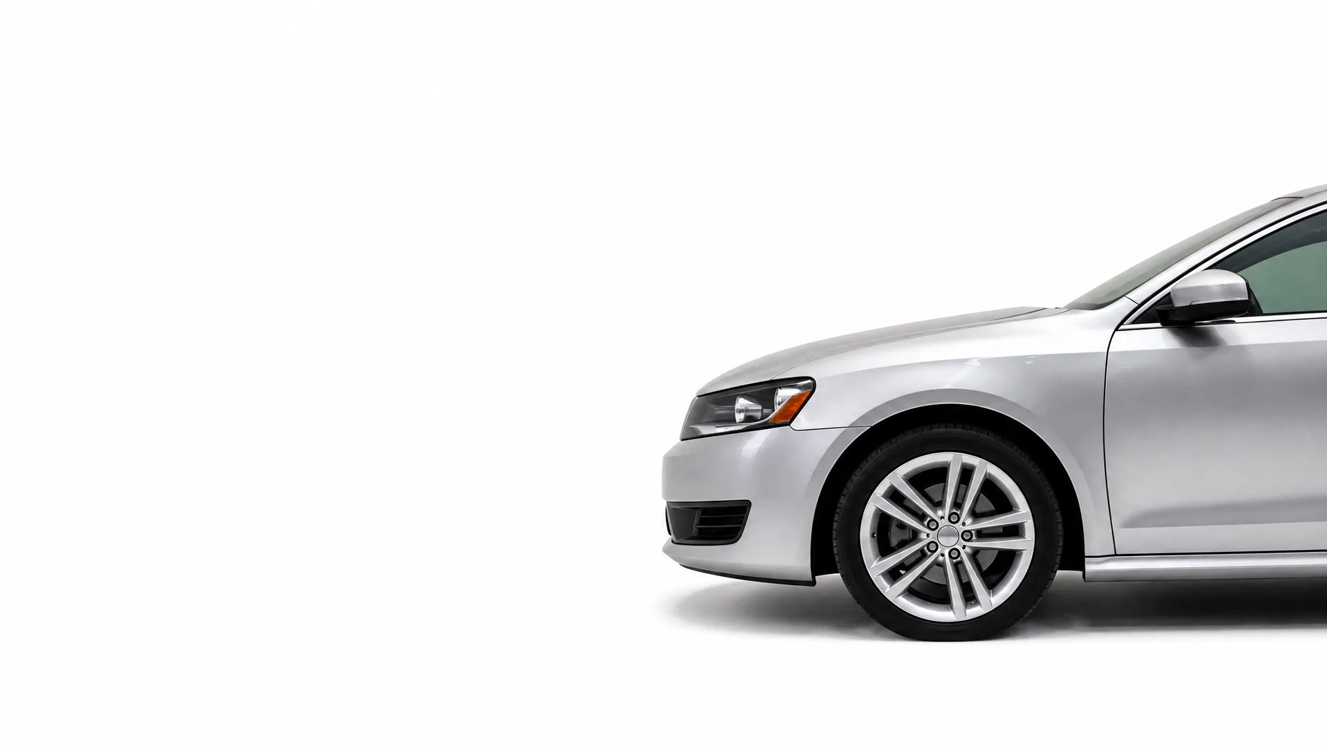 Front half of a silver four-door sedan photographed from the side against a plain white background, showing the headlight, front wheel with multi-spoke alloy rim, and side mirror.