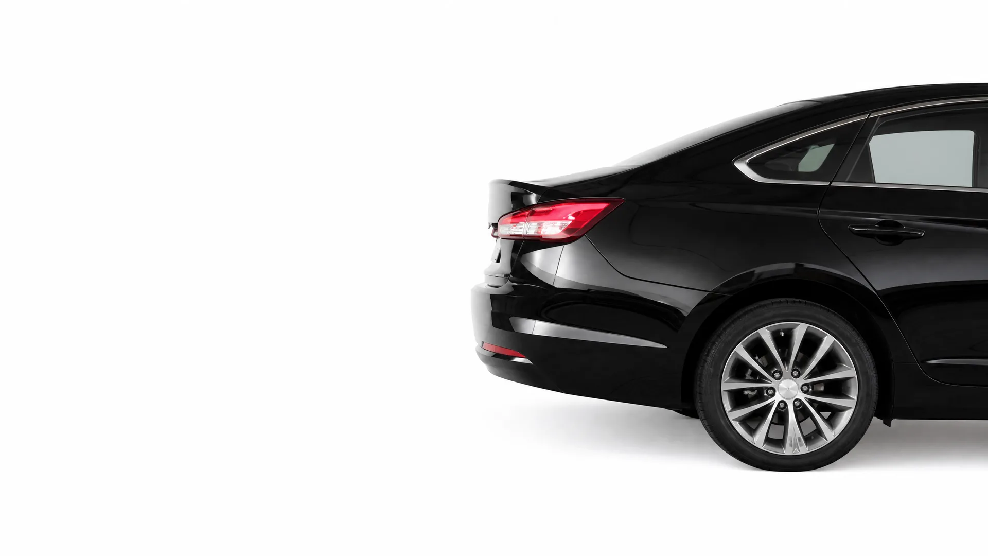 Rear three-quarter view of a black sedan's back half, including taillight, rear door and alloy wheel, against a plain white background.