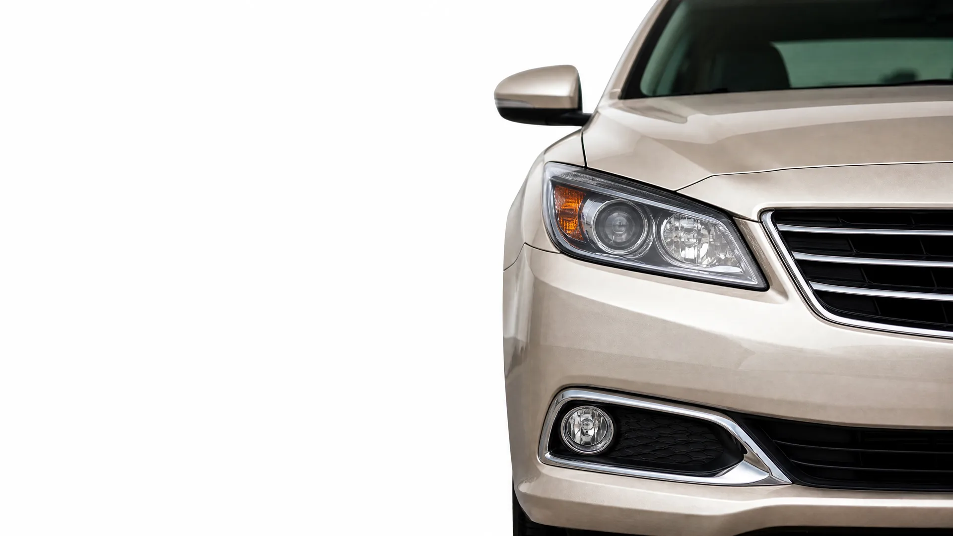 Front left portion of a beige sedan, showing the headlight, fog light, grille and side mirror, against a plain white background.