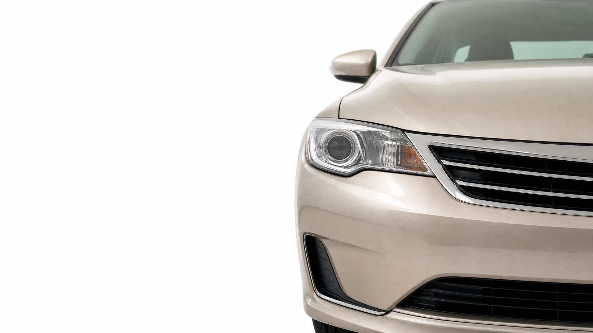 Front left portion of a beige sedan, showing the headlight, grille, bumper and side mirror, against a plain white background.