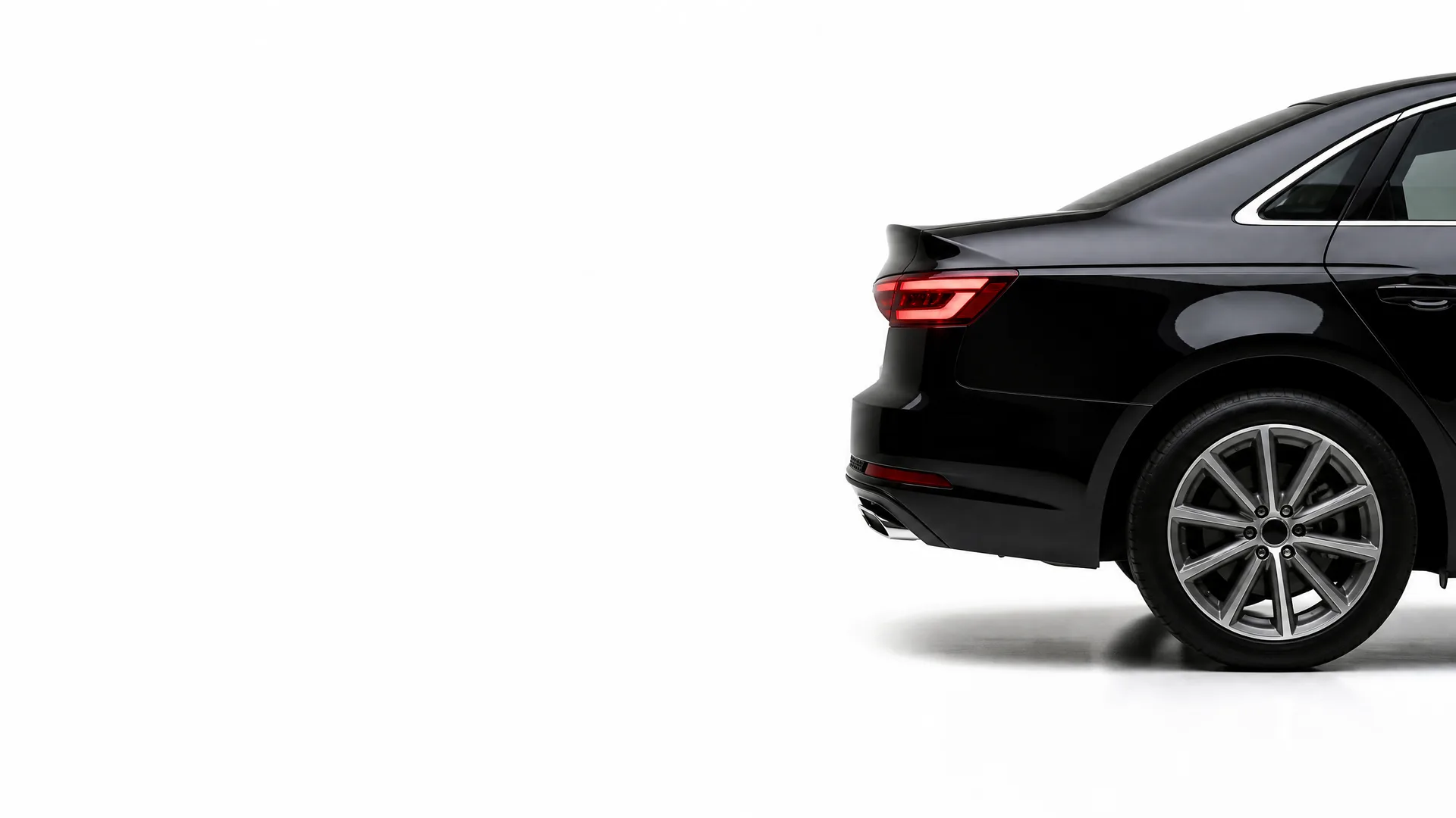 Rear section of a black sedan, showing the taillight, rear bumper, exhaust outlet and alloy wheel, against a plain white background.