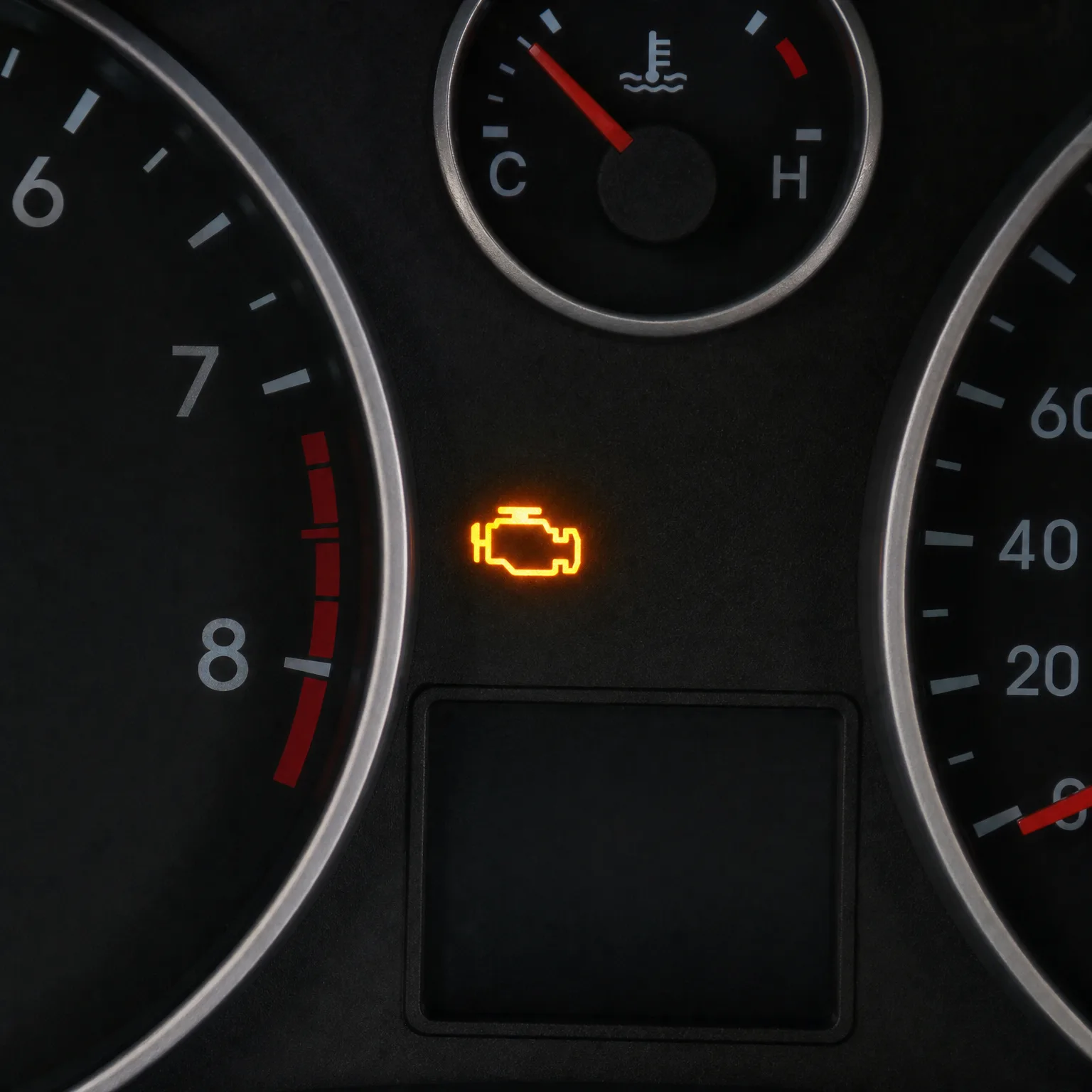Close-up of a car instrument cluster showing an illuminated amber engine-shaped warning light between a tachometer, a speedometer, and a coolant temperature gauge.