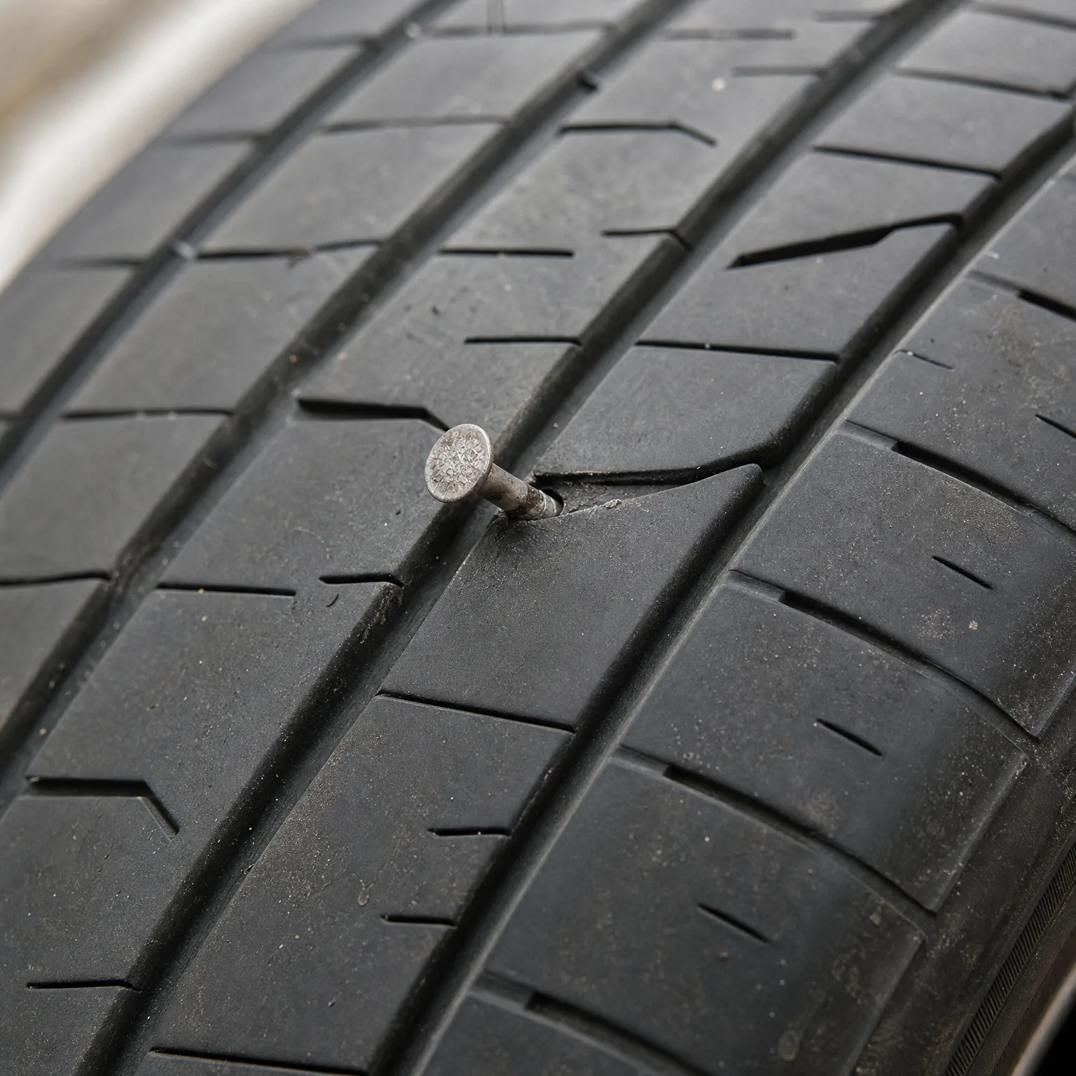 Close-up of a black tire tread with a nail embedded in the rubber between grooves.