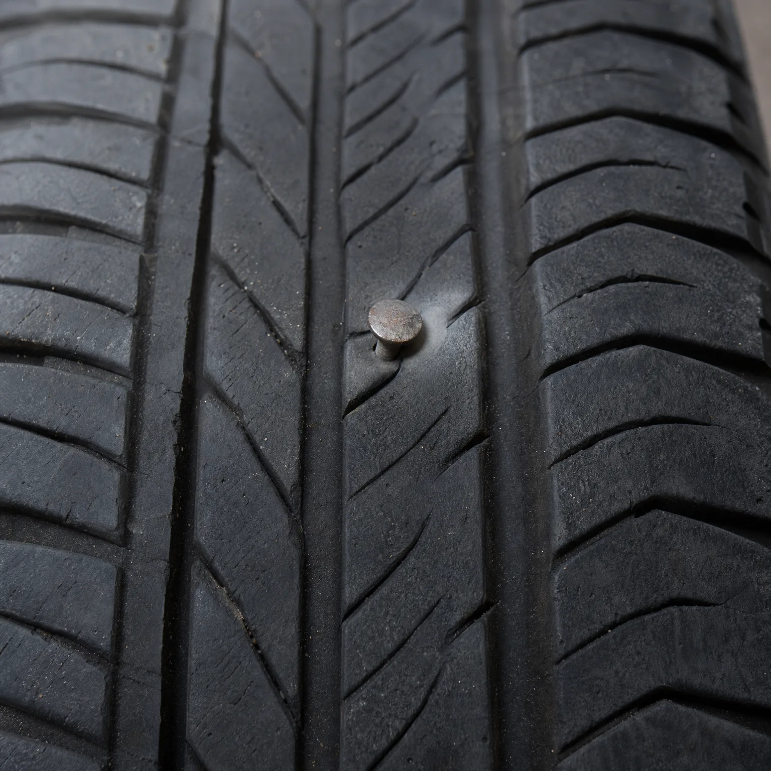 Close-up of a tire tread with a nail head embedded in the rubber between grooves.