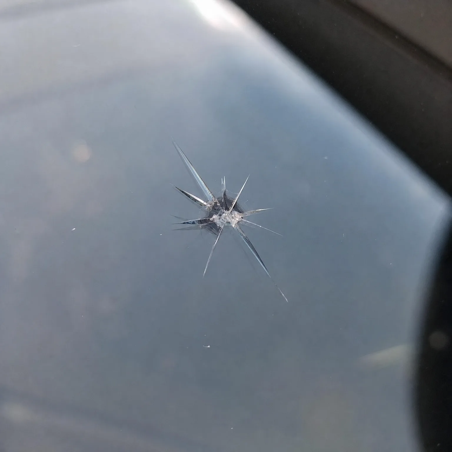 Close-up of a star-shaped chip in automotive glass, with cracks radiating outward from a small white impact point.