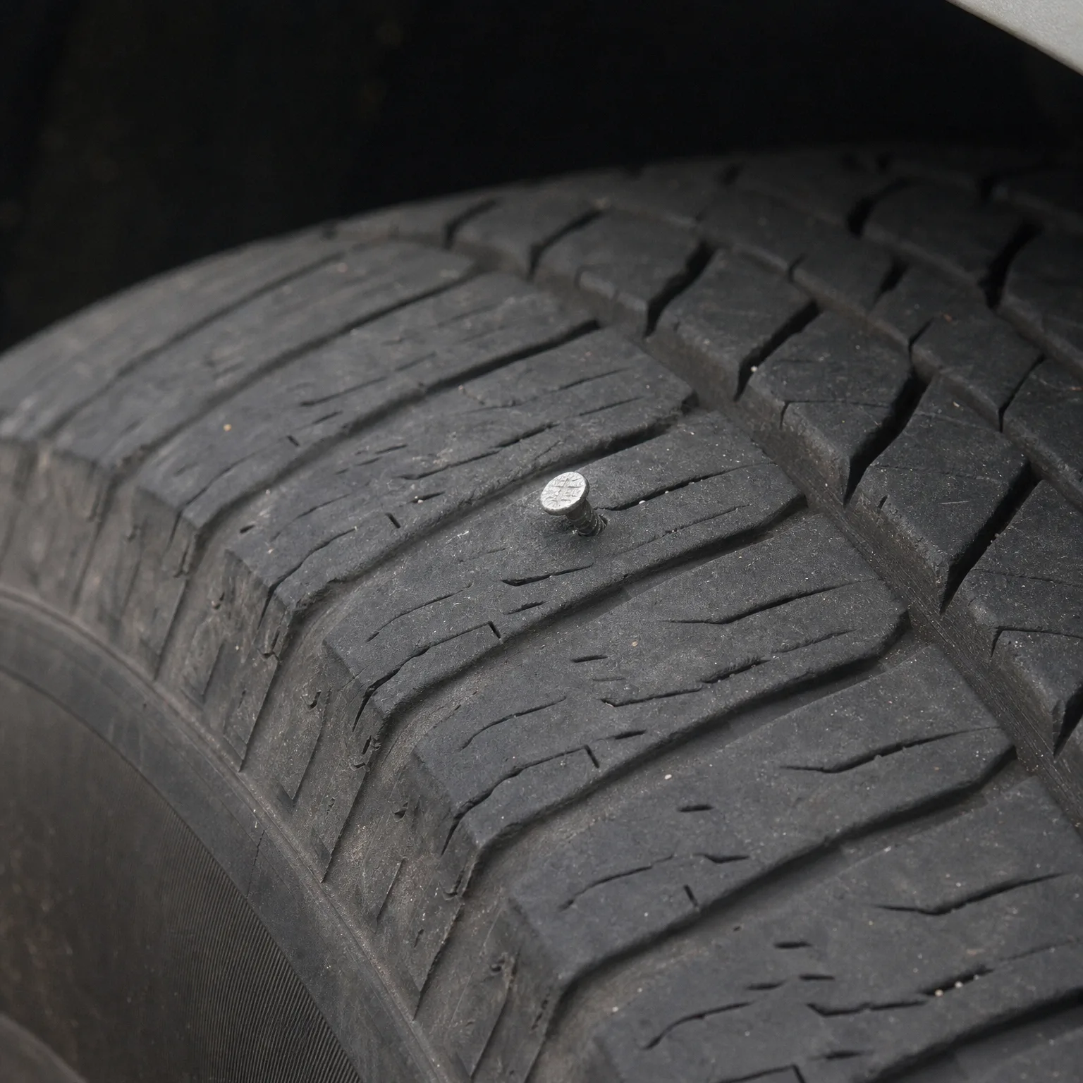 Close-up of a worn black tire tread with a nail head embedded in the rubber.