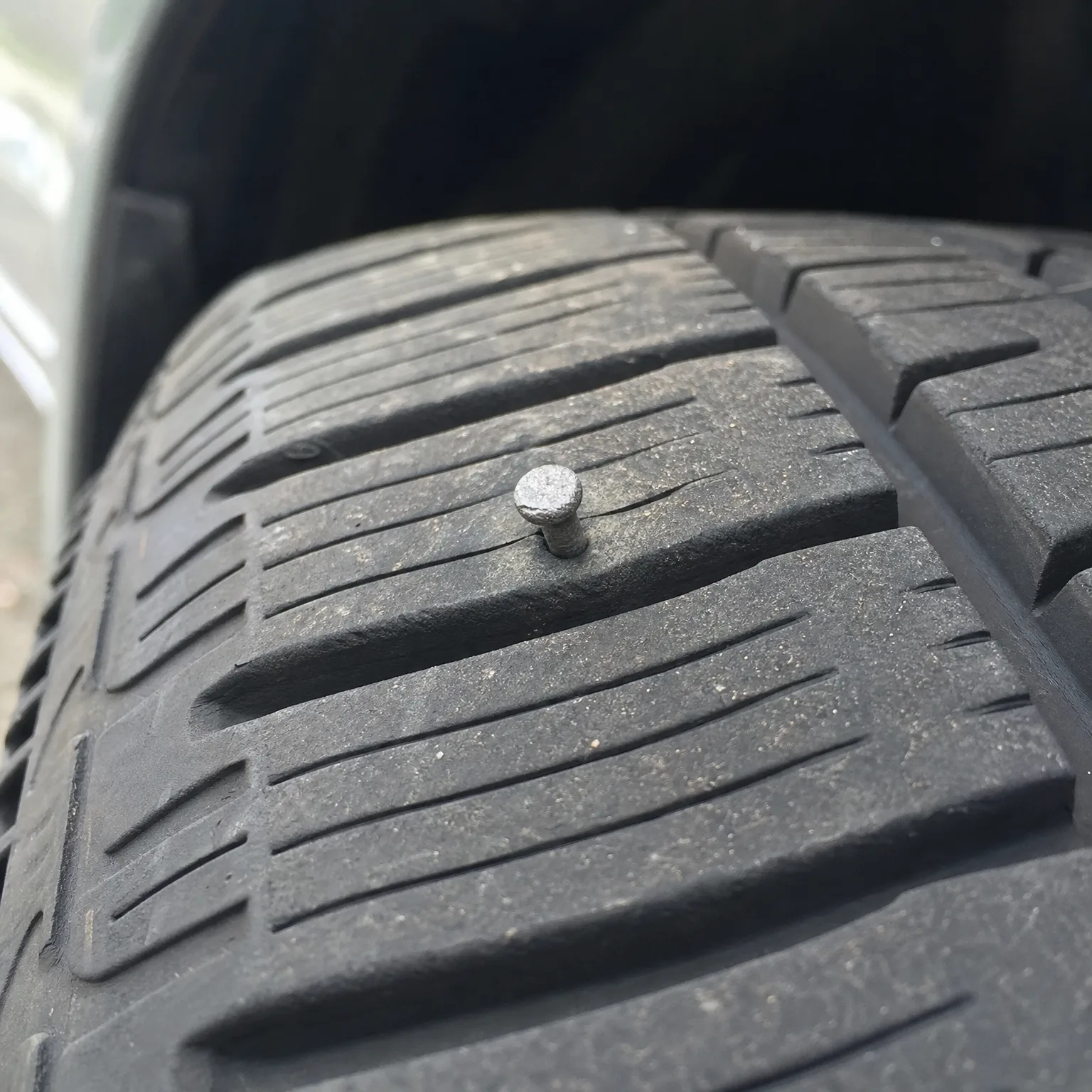 Close-up of a tire tread with a nail head embedded in the rubber between grooves.
