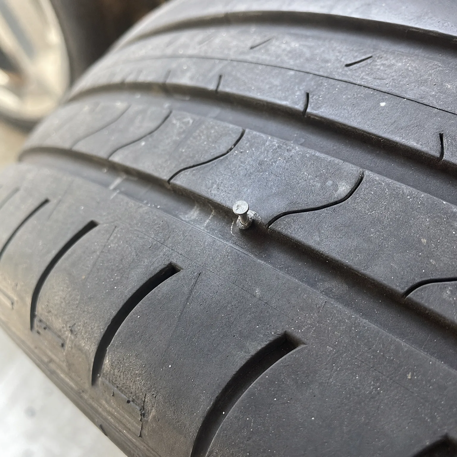 Close-up of a car tyre tread with a nail head embedded in the rubber between grooves.