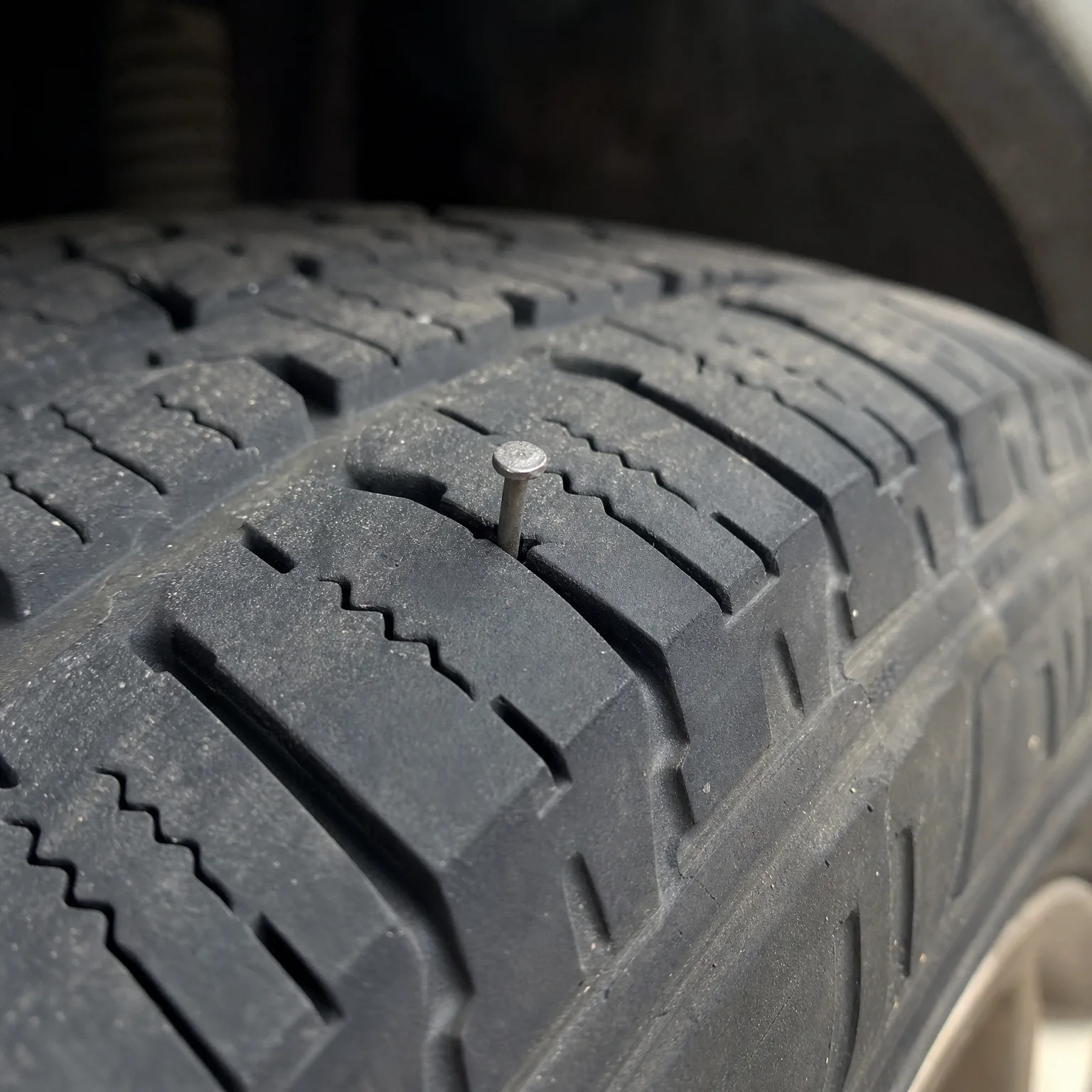 Close-up of a tire tread with a nail embedded in the rubber between grooves.