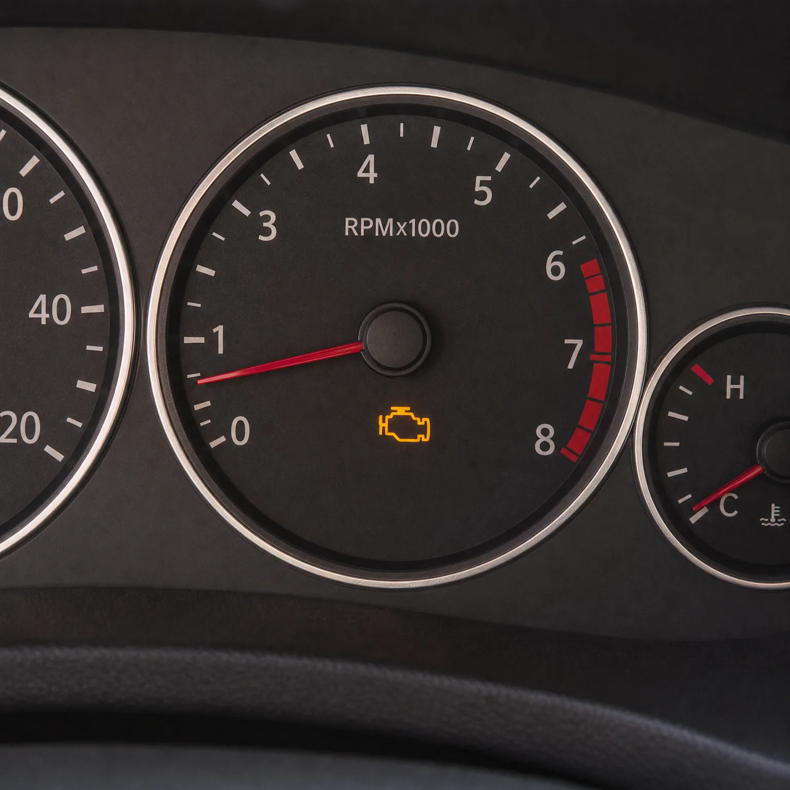 Close-up of a car instrument cluster showing a tachometer marked RPMx1000 with the needle near zero, an illuminated amber check-engine light, a partial speedometer at left and a coolant temperature gauge at right.