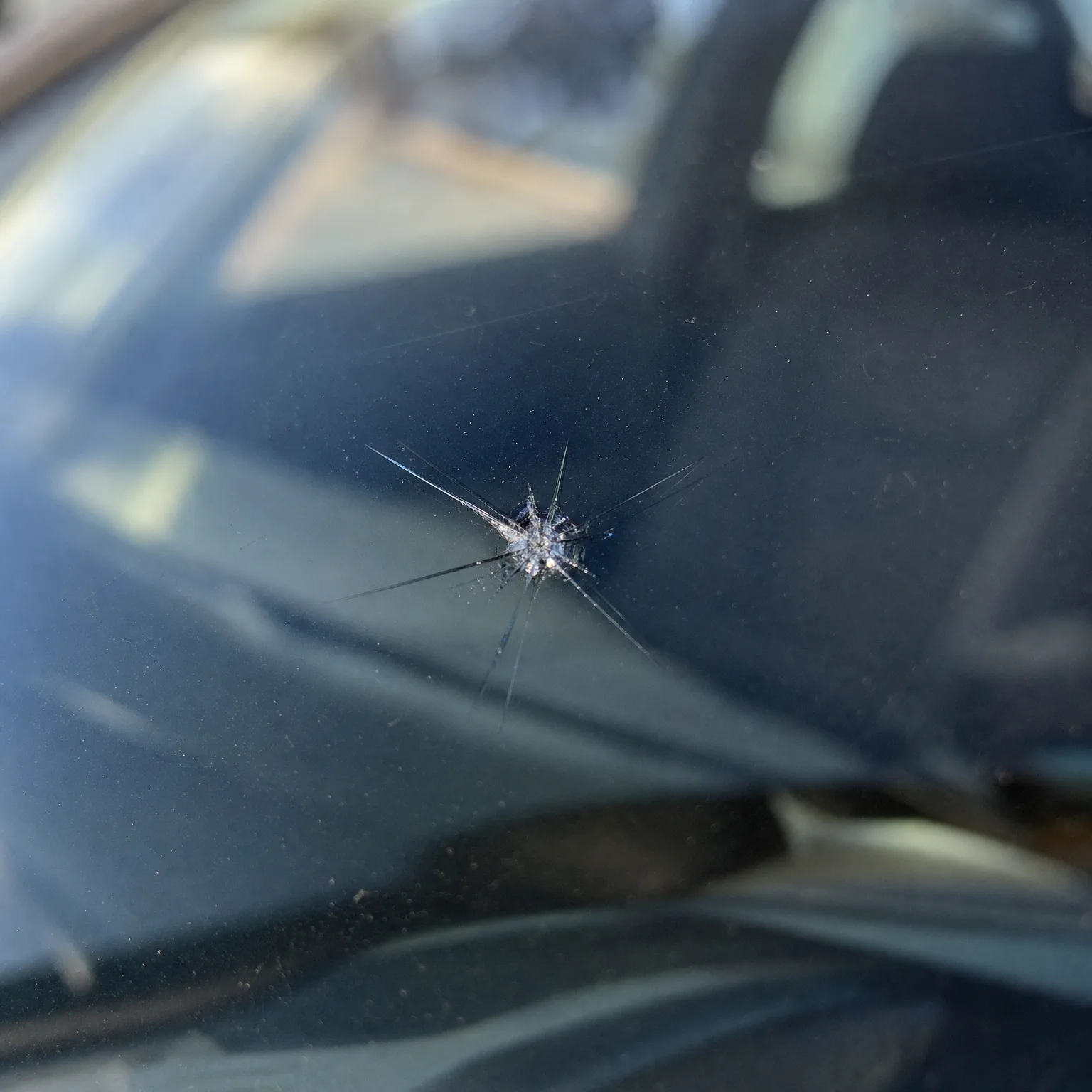 Close-up of a star-shaped chip in a vehicle windshield with cracks radiating from the impact point, with dark interior and reflections behind the glass.