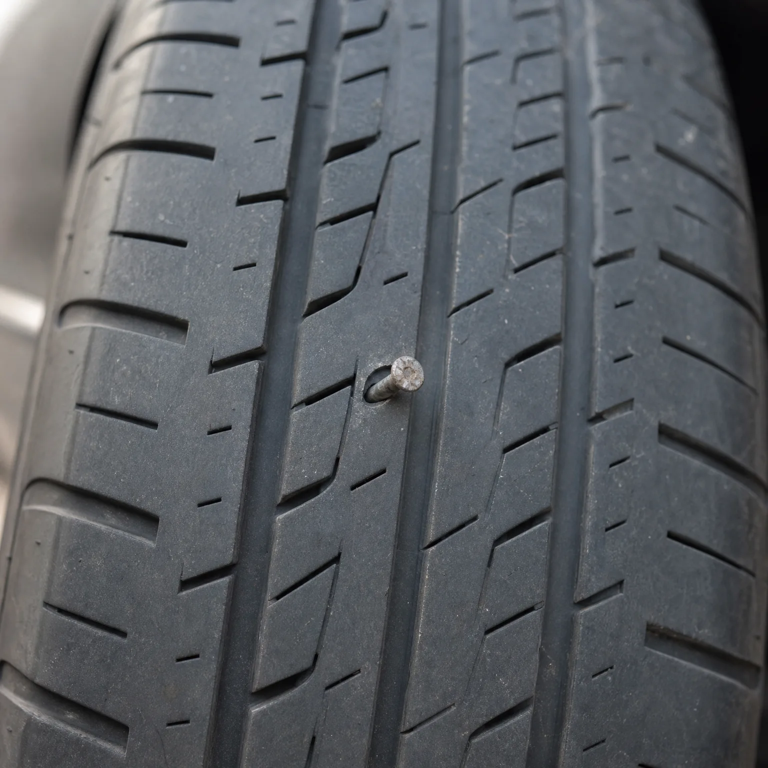 Close-up of a tire tread with a screw head embedded in the rubber between grooves.
