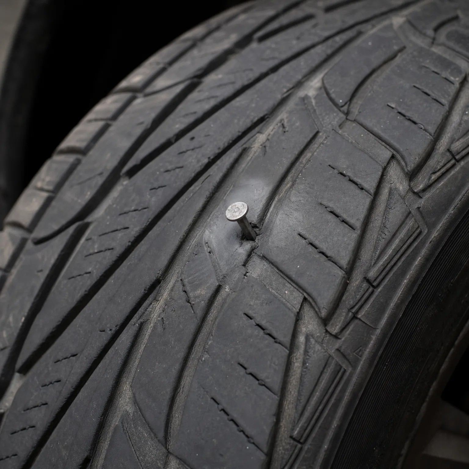 Close-up of a black tire tread with a nail embedded in the rubber between grooves.