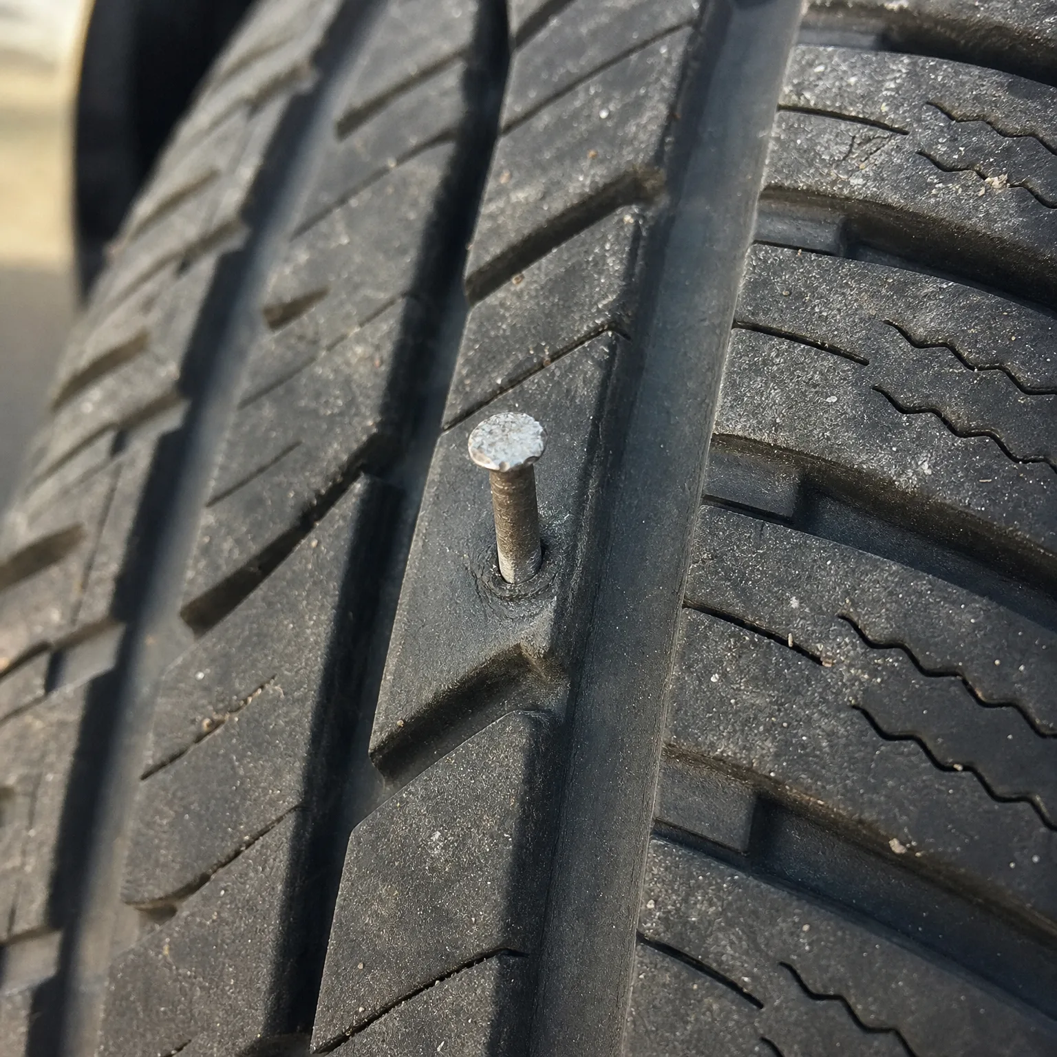 Close-up of a tire tread with a nail embedded in a groove between tread blocks.