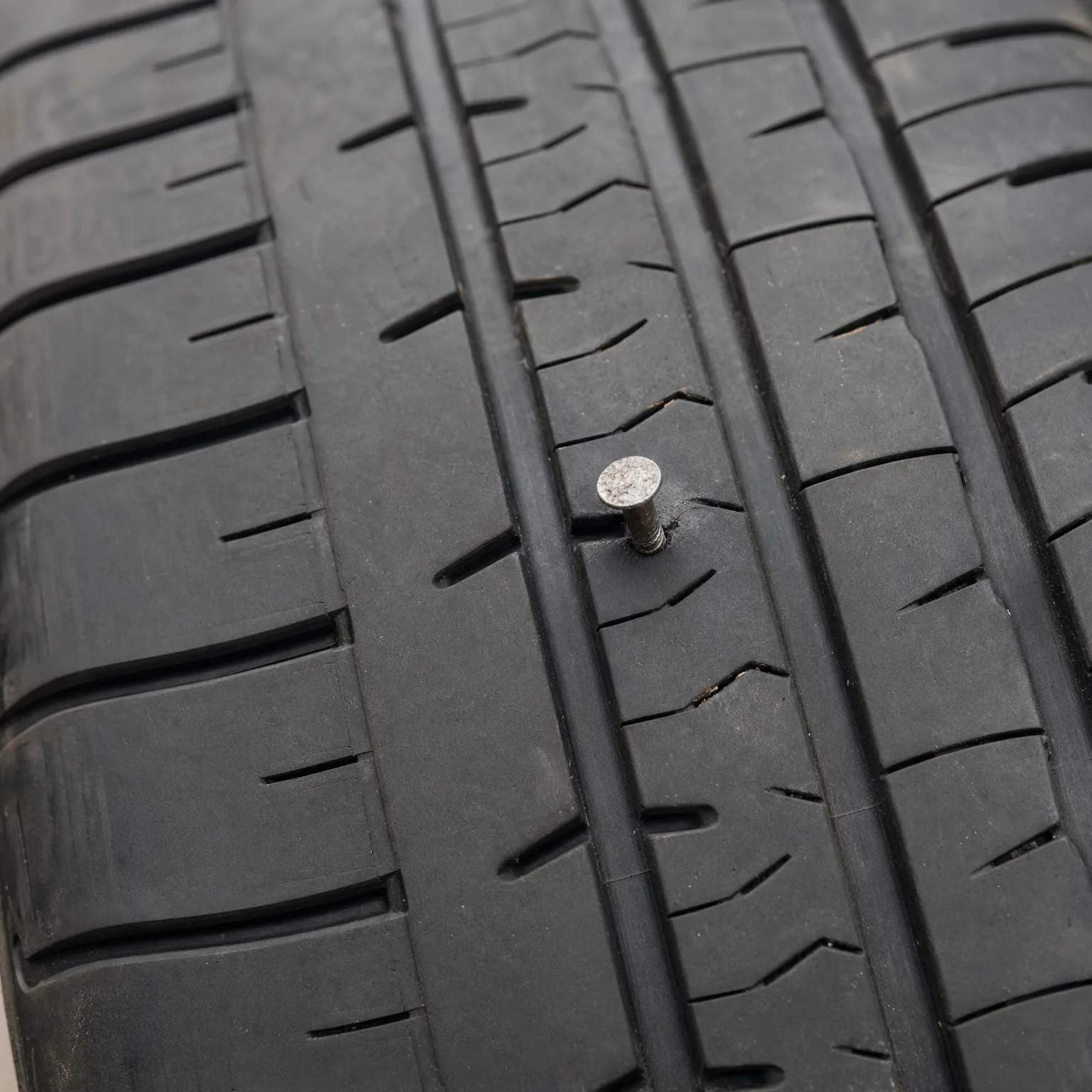 Close-up of a black tire tread with a nail embedded in the rubber between two grooves.