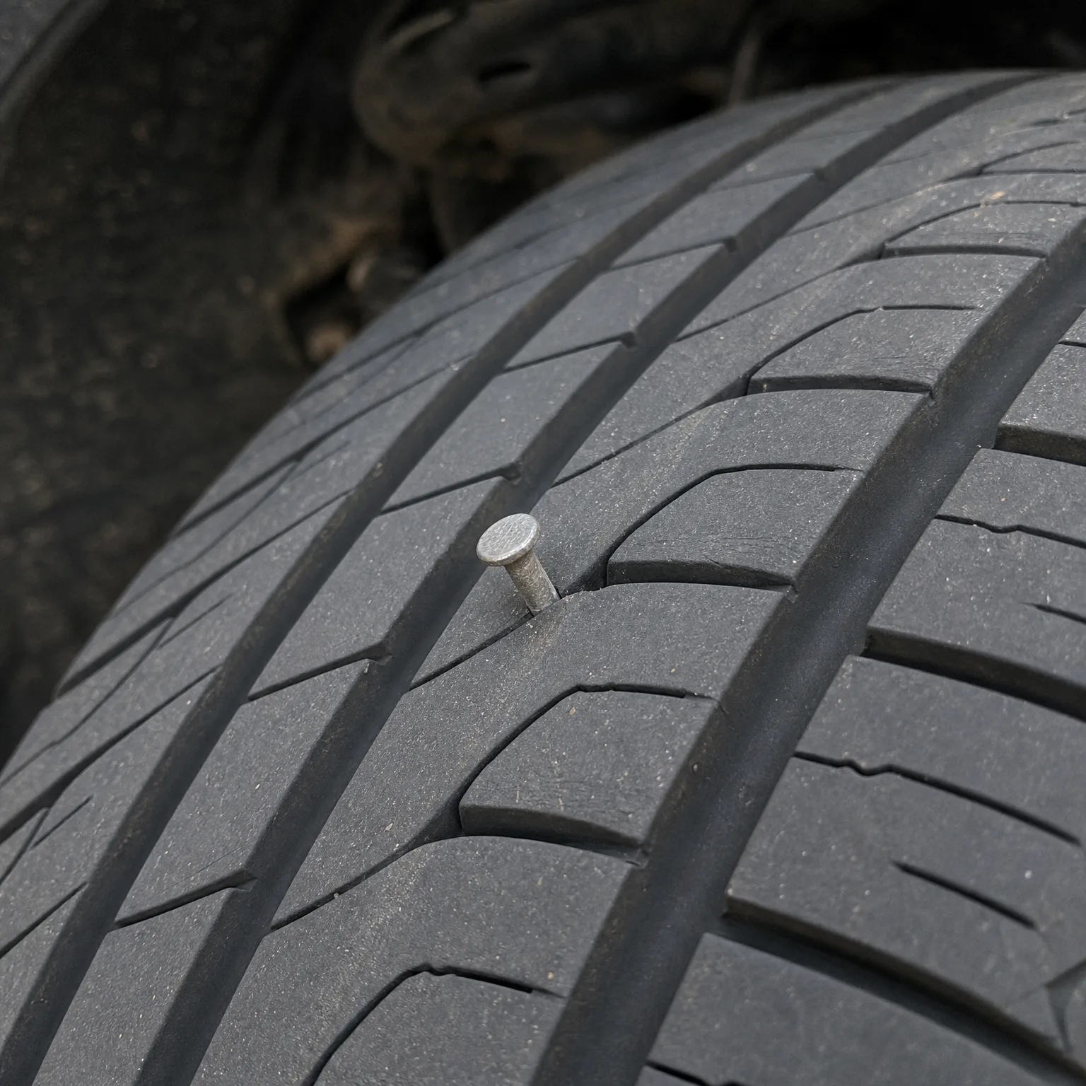 Close-up of a tire tread with a metal nail head embedded in a groove between tread blocks.
