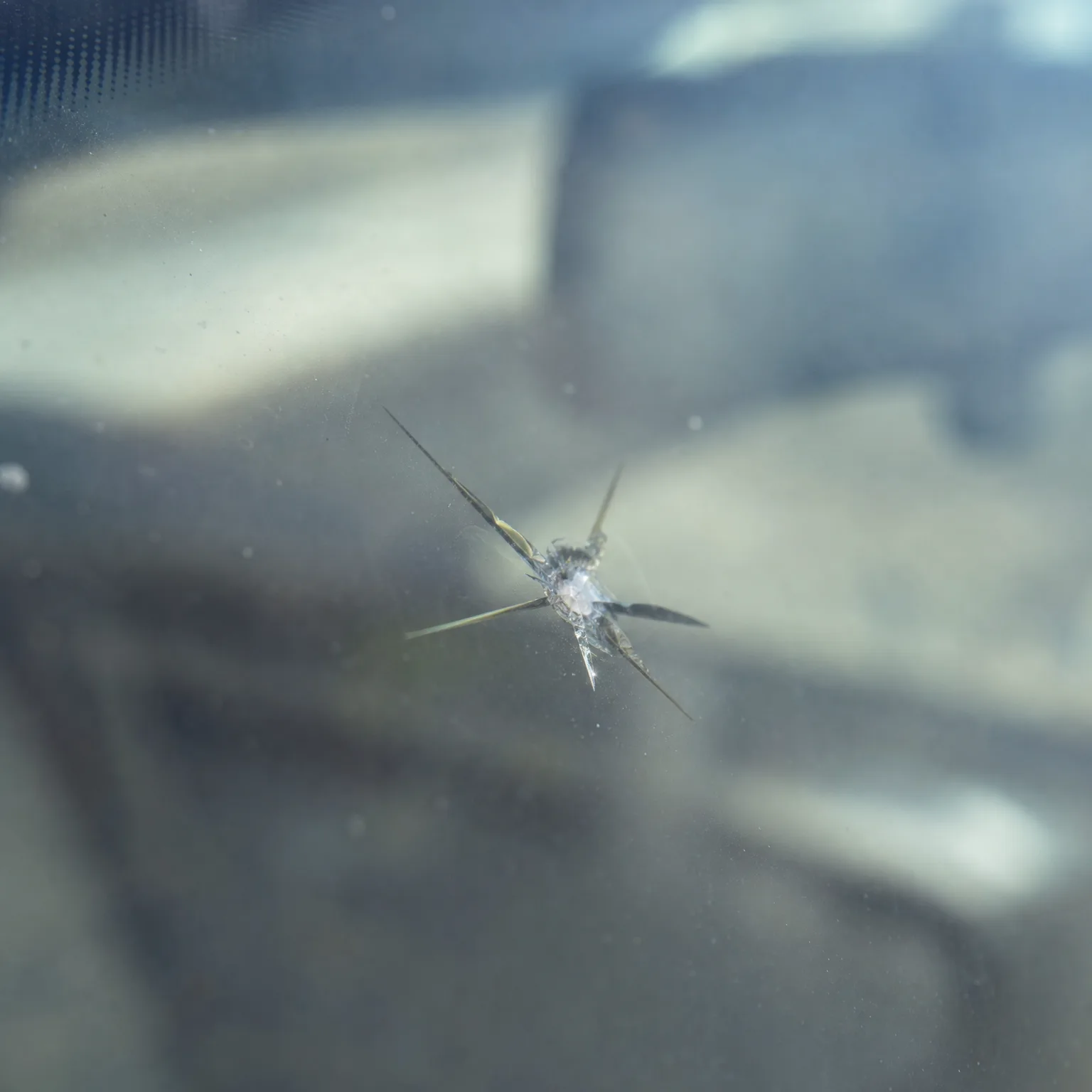 Close-up of a star-shaped chip in glass with several radiating cracks, against a blurred background.