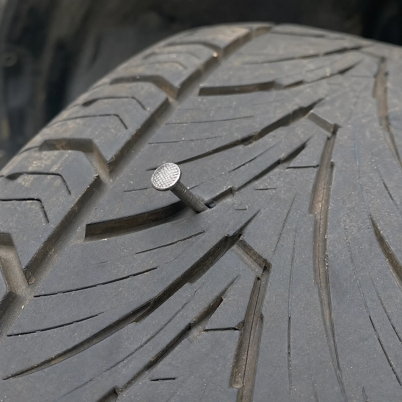 Close-up of a worn tire tread with a nail embedded in the rubber.