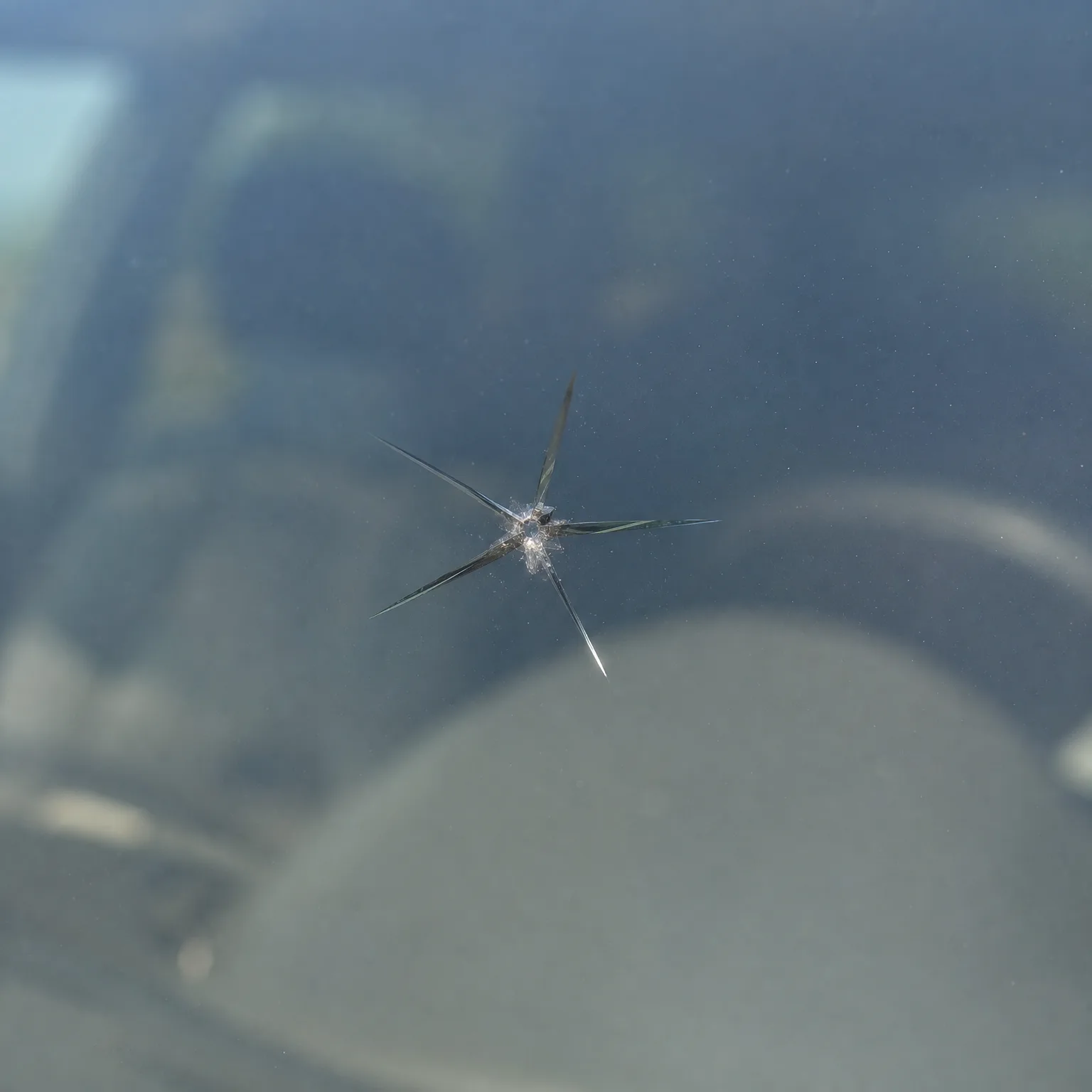 Close-up of a star-shaped chip with radiating cracks in a vehicle windshield, with the blurred dashboard interior visible behind the glass.