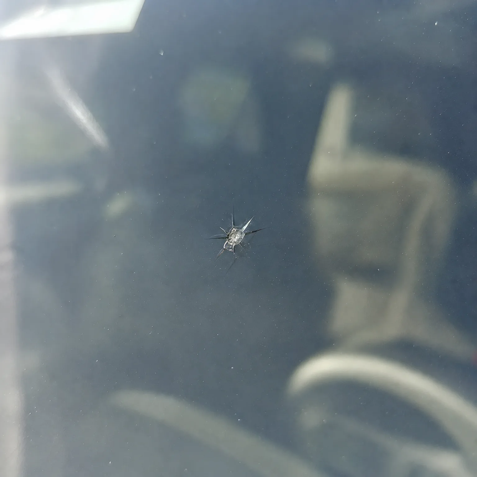 Close-up of a small star-shaped chip with radiating cracks in a vehicle windshield, with the dark car interior blurred behind the glass.