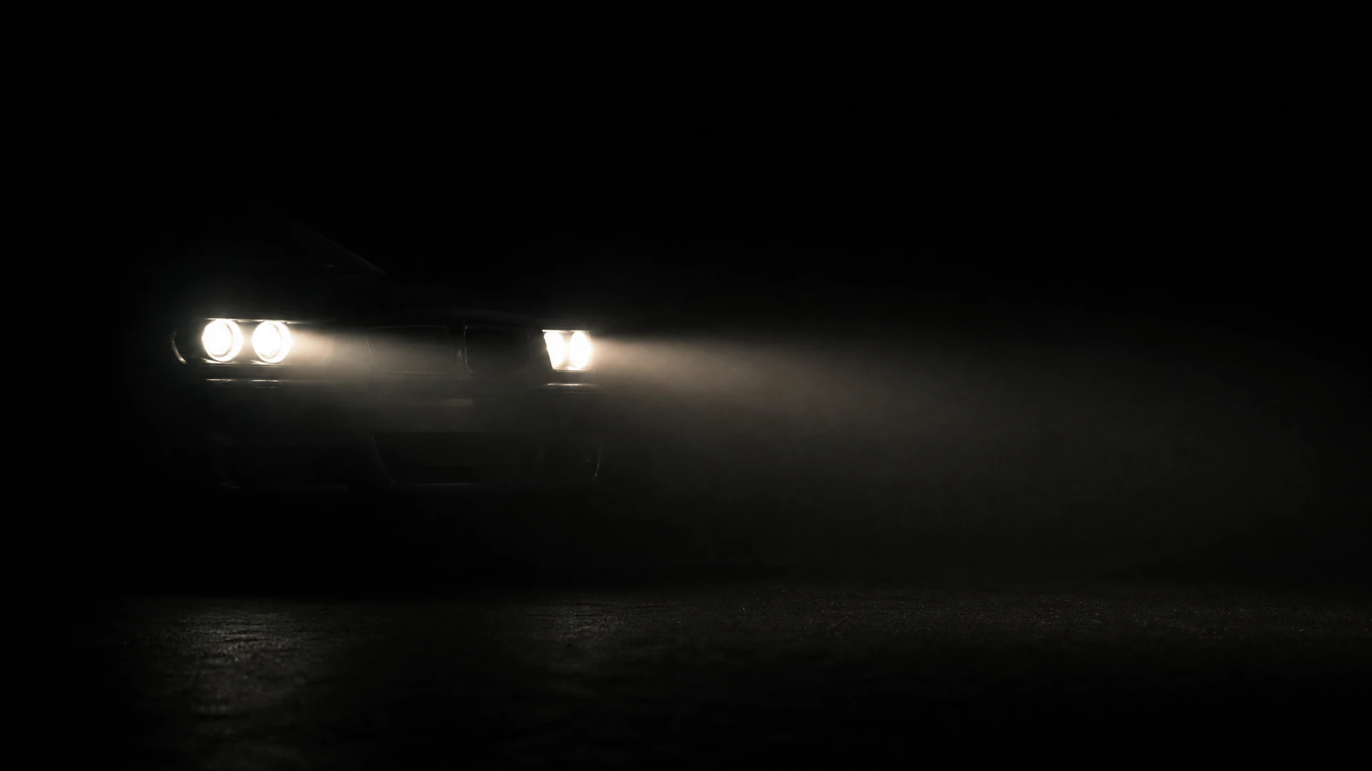 A car with glowing headlights emerging through fog in a dark environment.