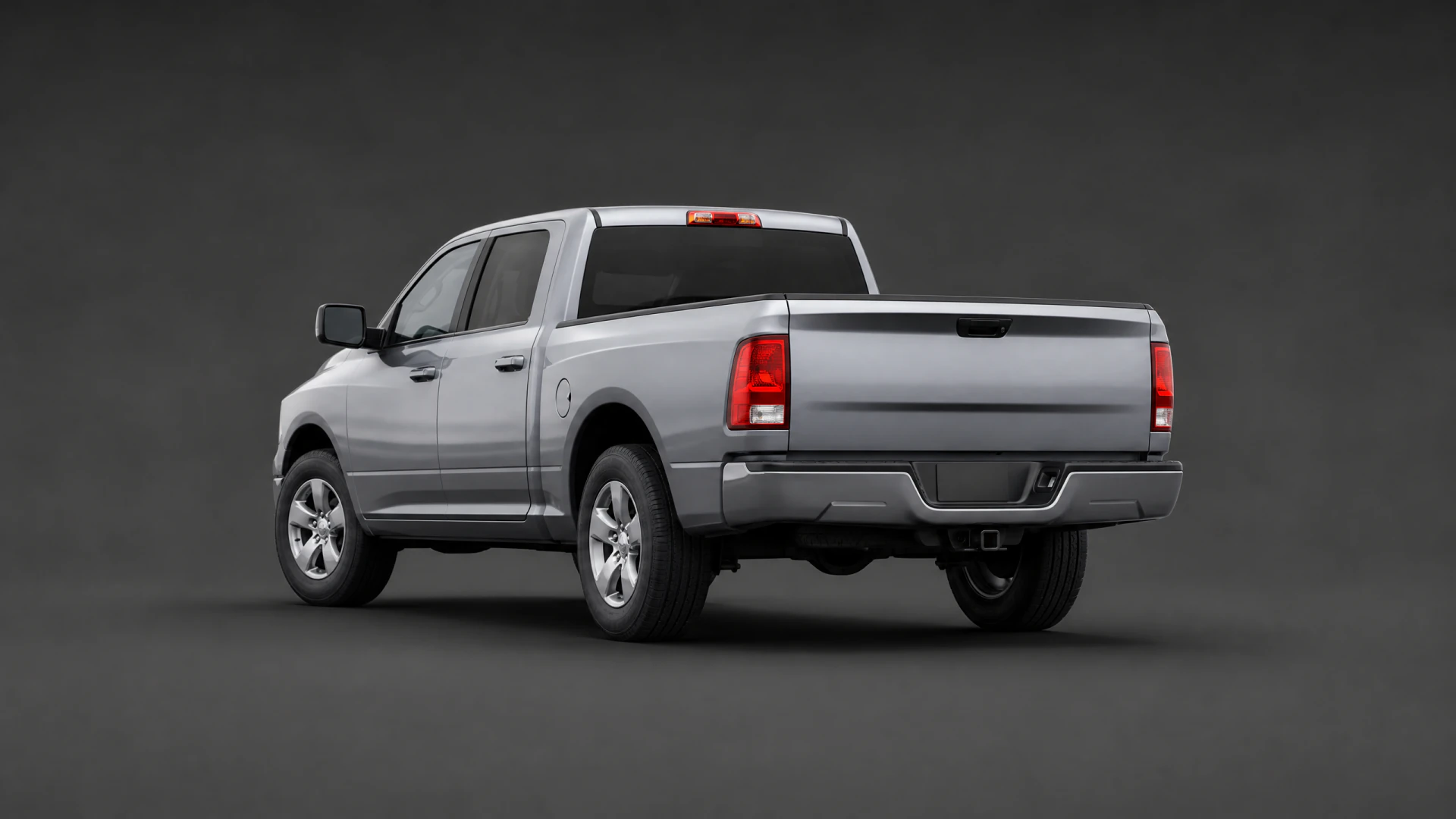 A silver crew-cab pickup truck shown from the rear three-quarter view in a dark studio setting.