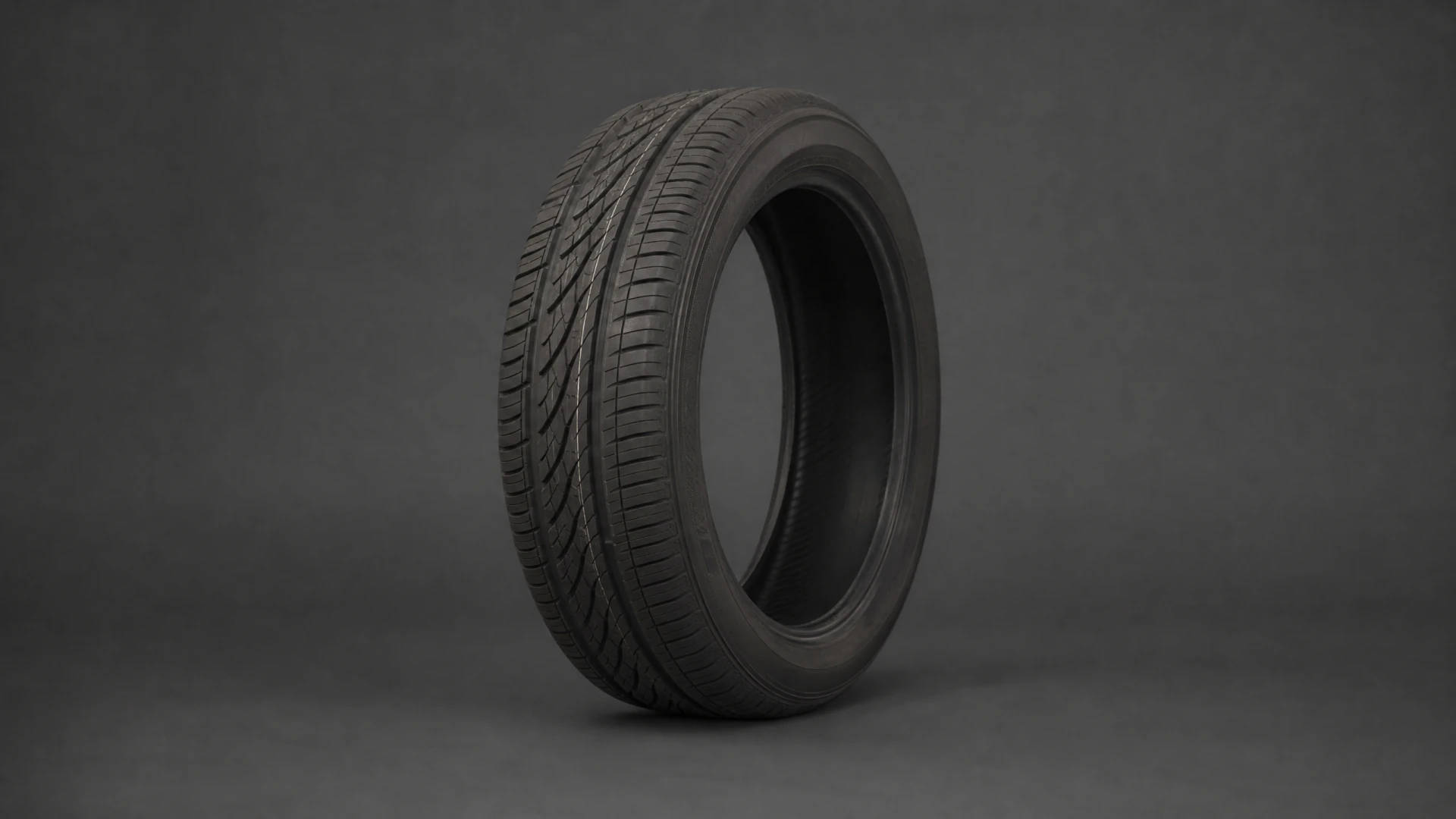 A black automobile tire with an asymmetric tread pattern stands upright against a dark gray background.