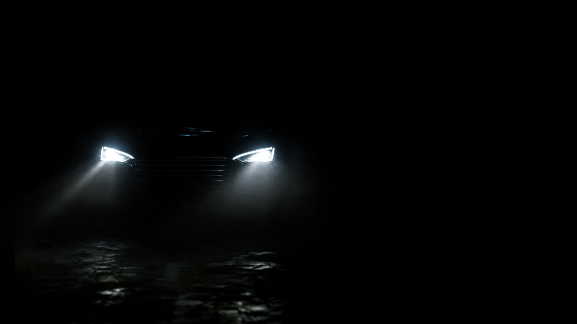 The front of a car emerges from darkness, its two bright white headlights casting light onto a wet cobblestone surface.