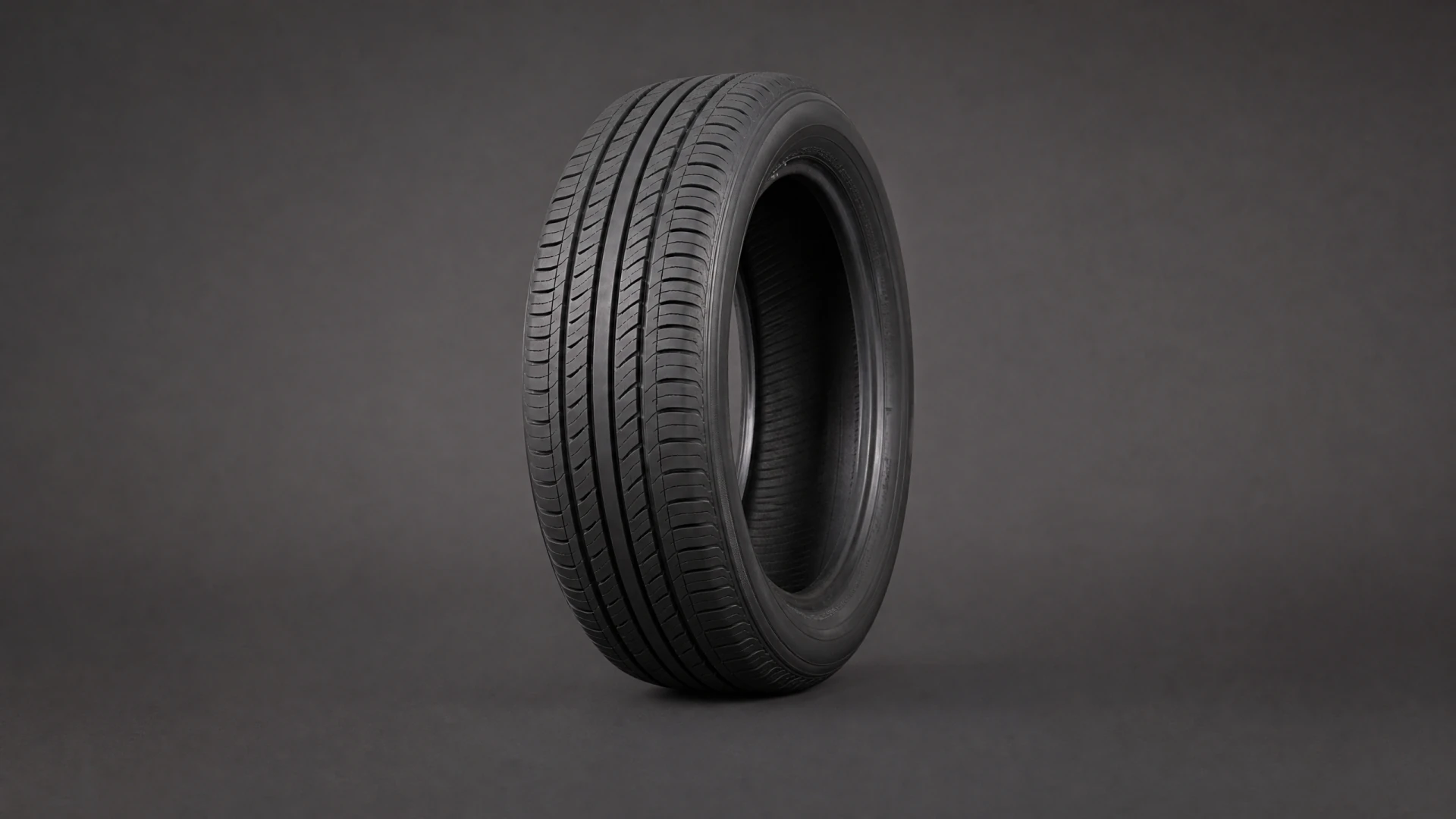A black car tire with diagonal tread grooves stands upright against a dark gray background.